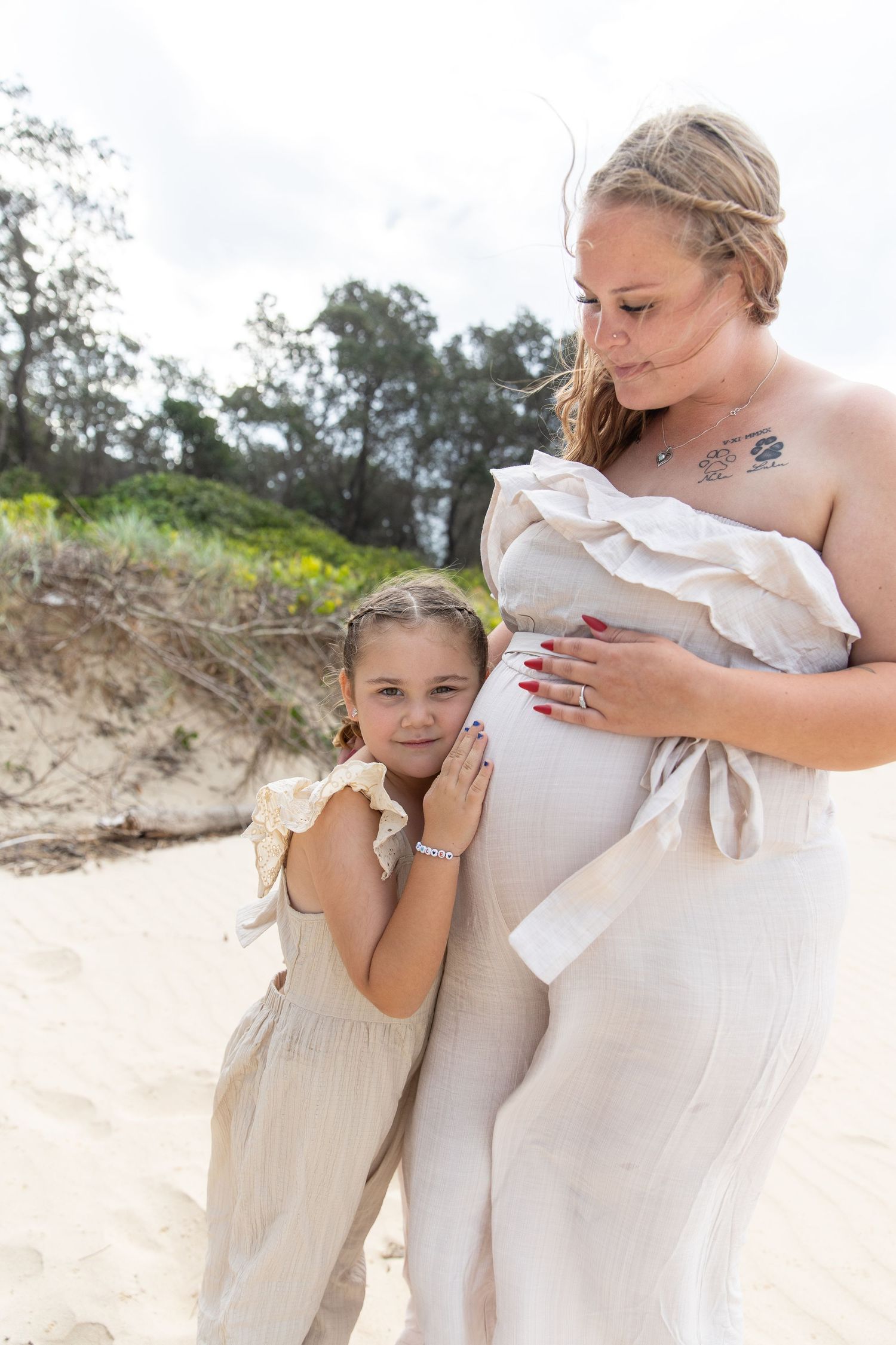 A tender moment captured on a beach with light beige dresses and soft natural lighting.