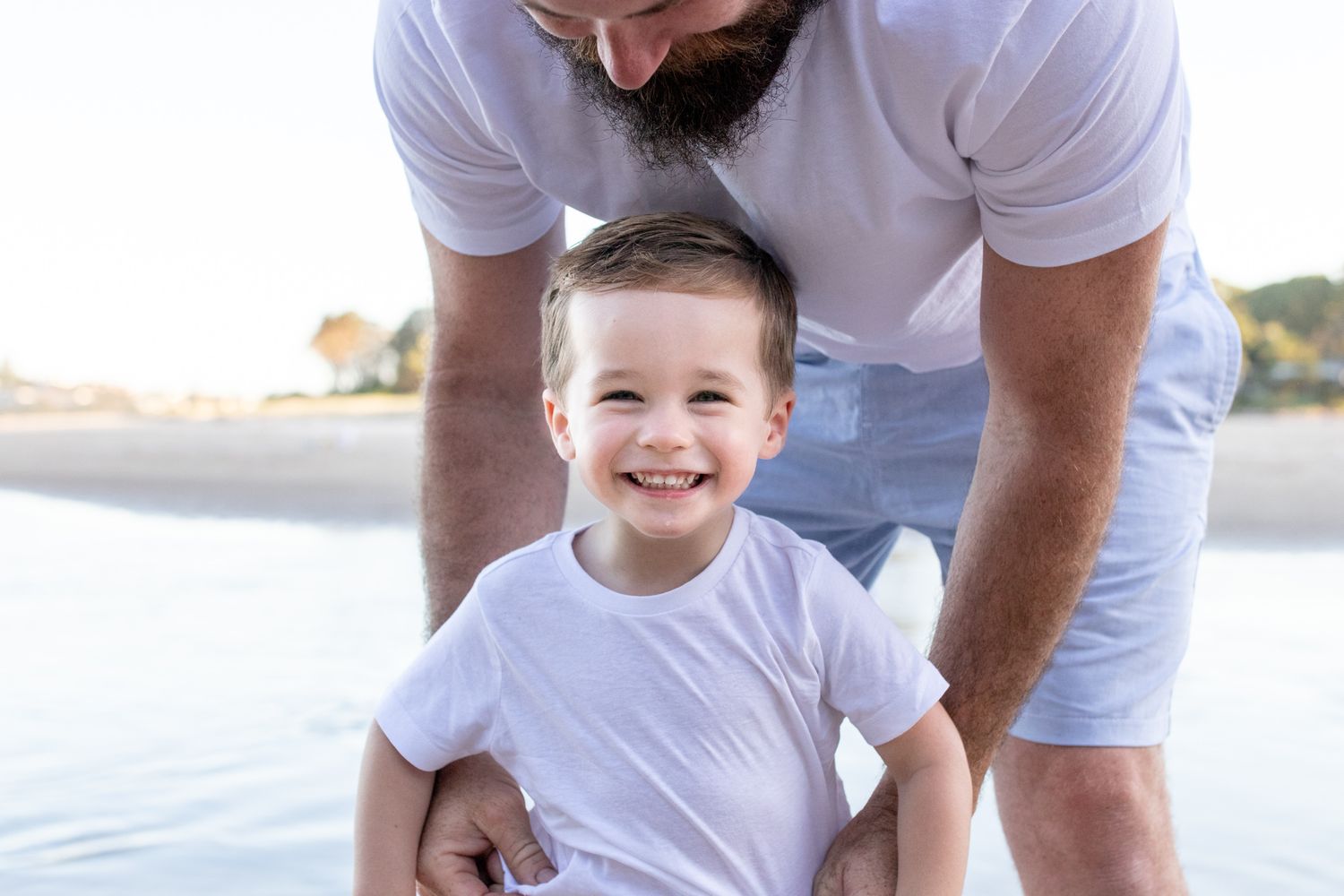 Family playing and laughing together at the beach in white casual attire.