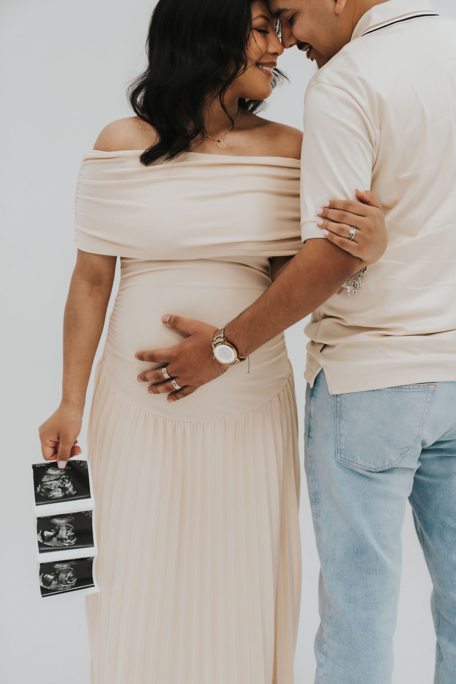 Couple in cream colored outfits holding ultrasound photos during pregnancy announcement photoshoot.