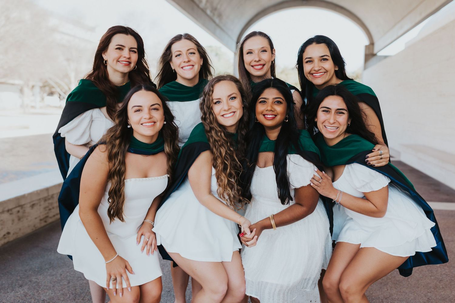 A cheerful group wearing matching green and white outfits pose together under an arched walkway.