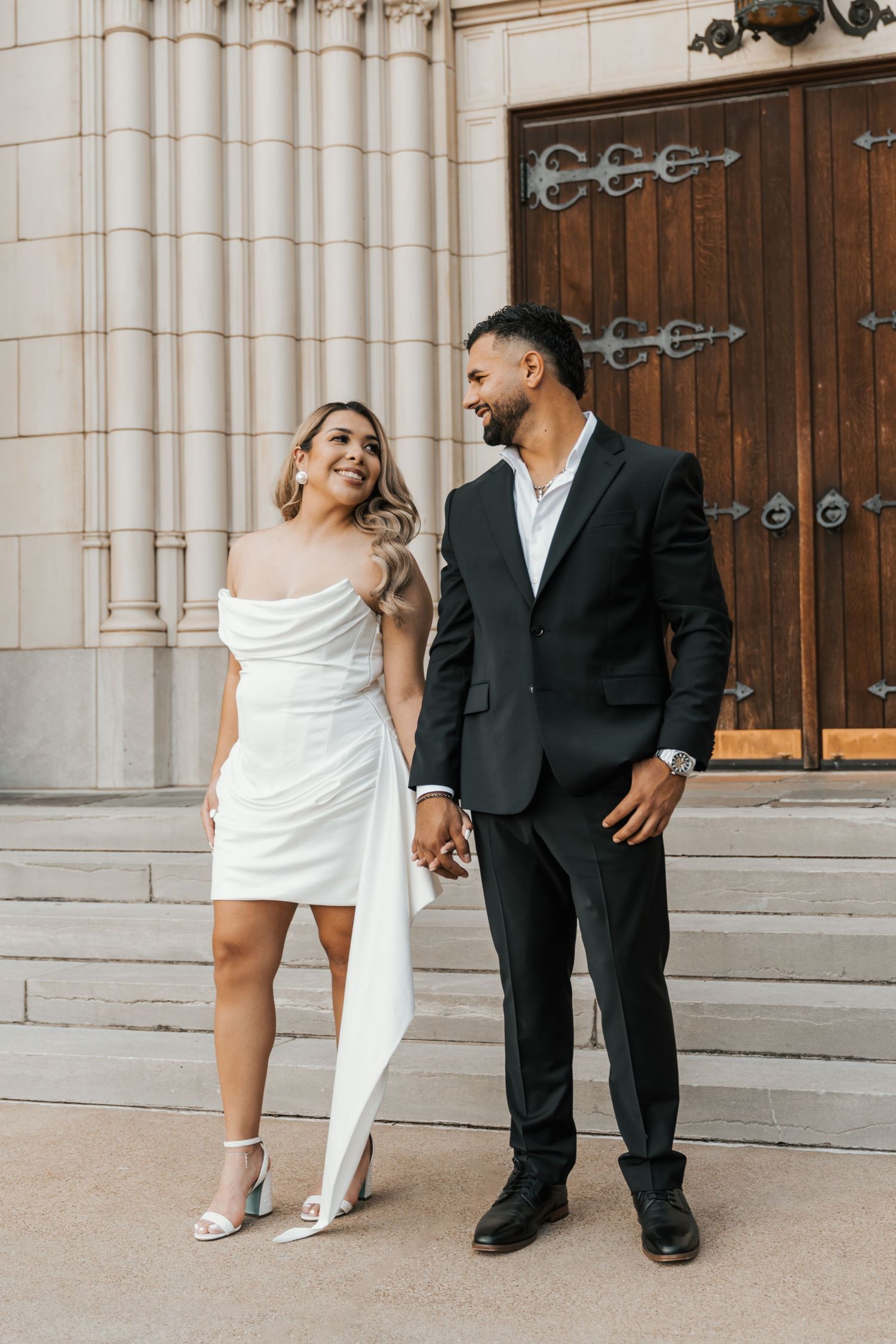 A playful wedding couple poses on church steps in a series of candid moments showing white dress and black suit.