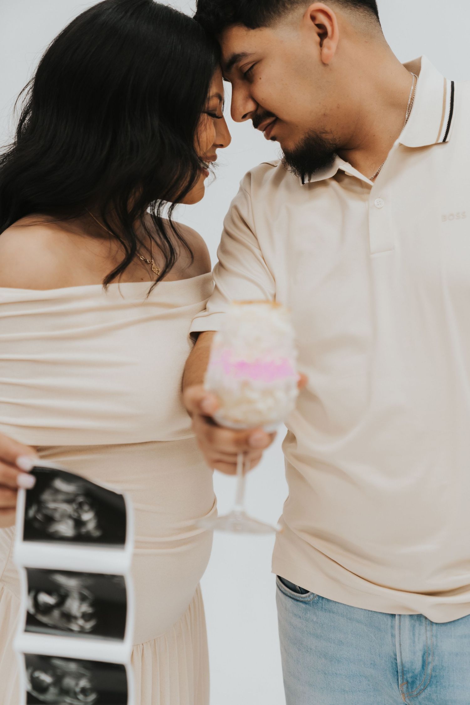 A couple in neutral tones shares tender moments in a pregnancy announcement photoshoot with ultrasound pictures.