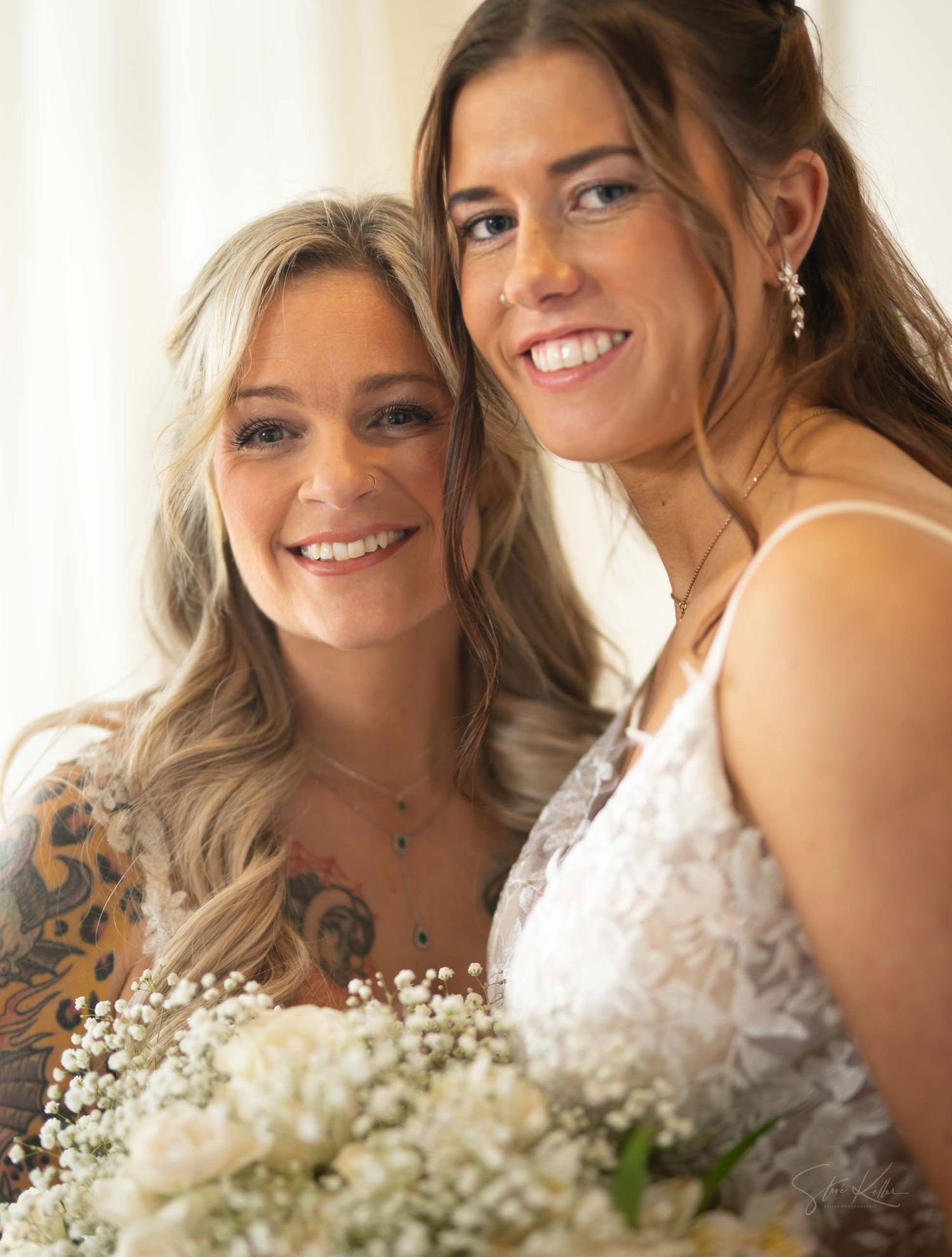 Two people in wedding attire pose together with white flowers and joyful expressions.