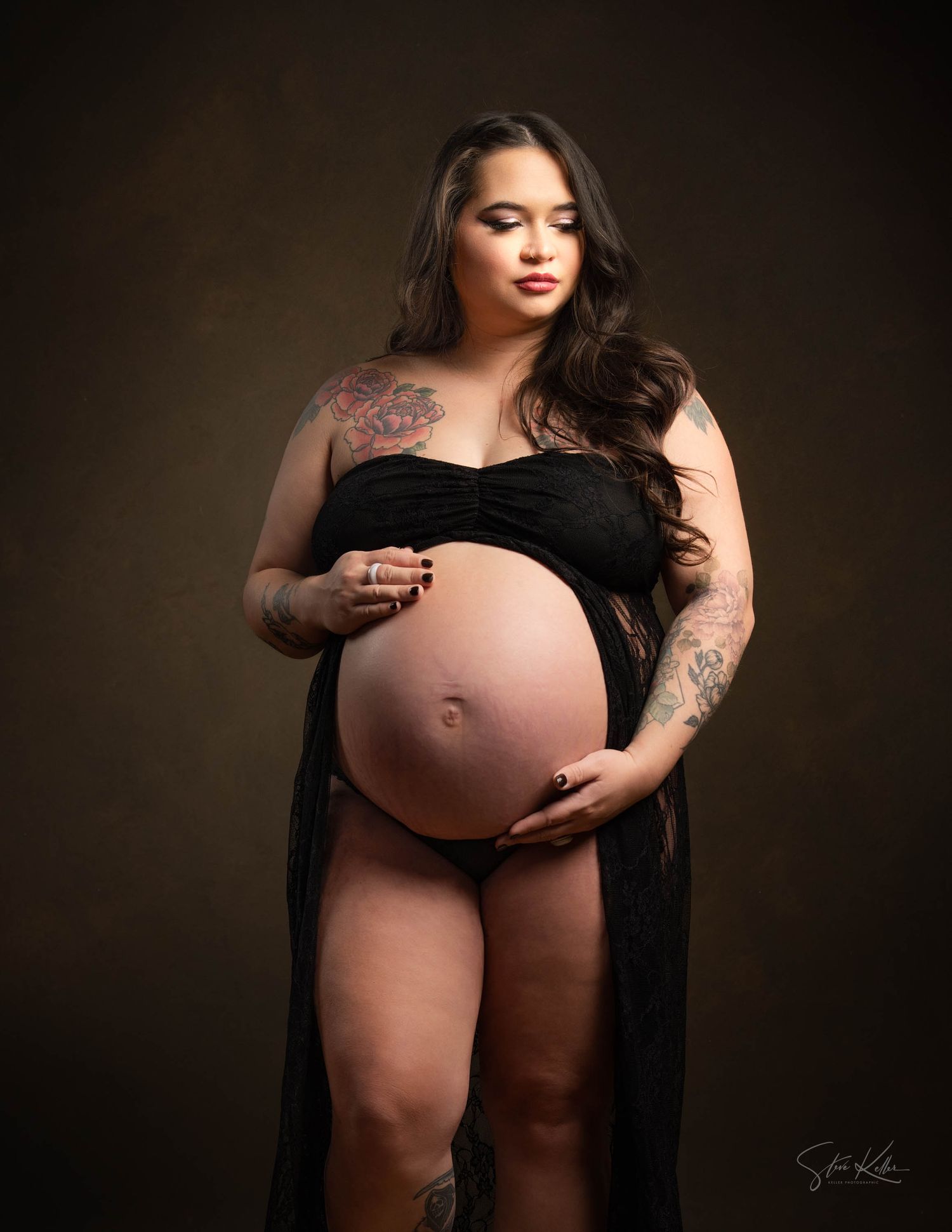 Artistic maternity portrait highlighting pregnancy with black dress and tattoo details.