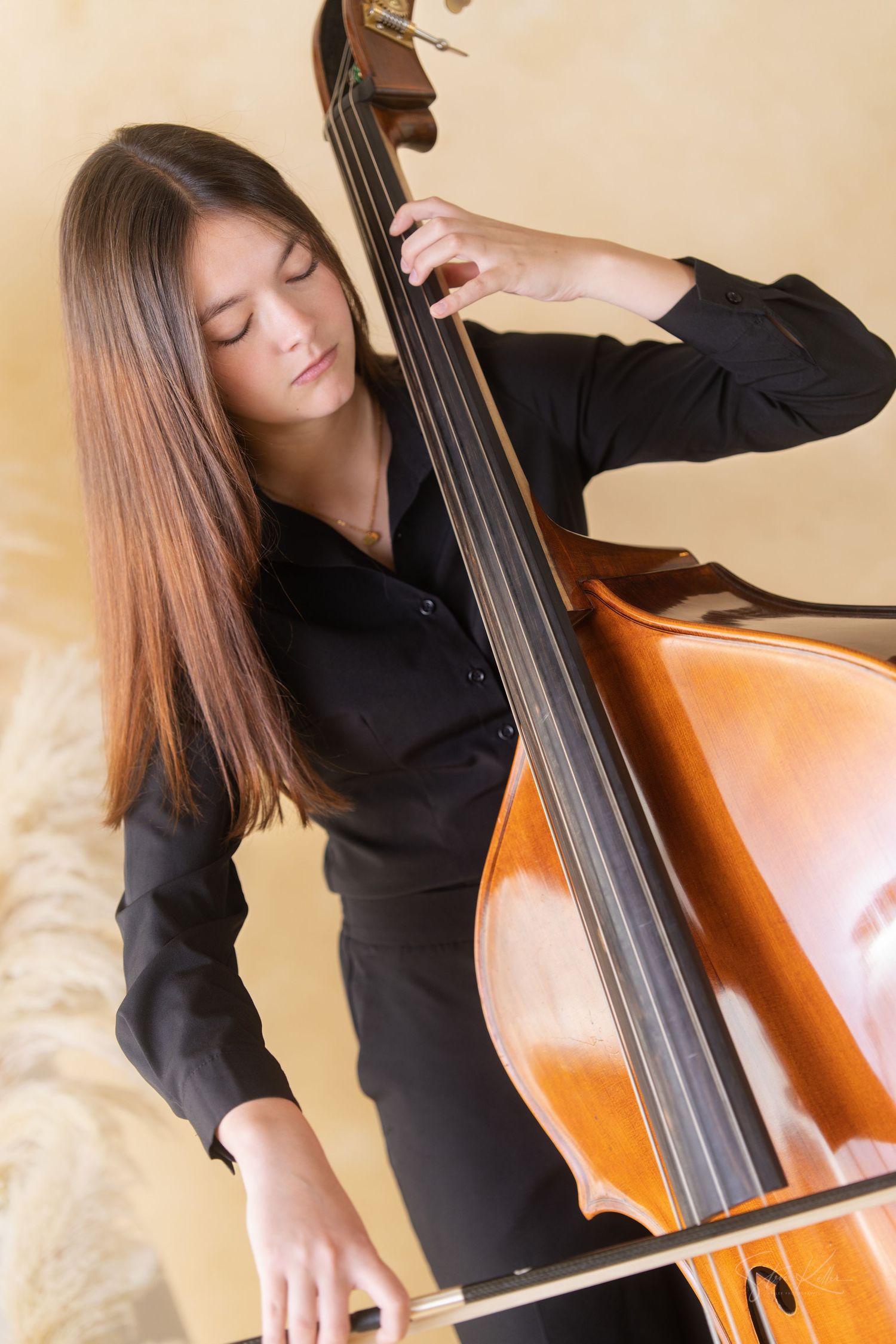 Musician plays upright double bass in elegant black attire with passionate expression against warm background.
