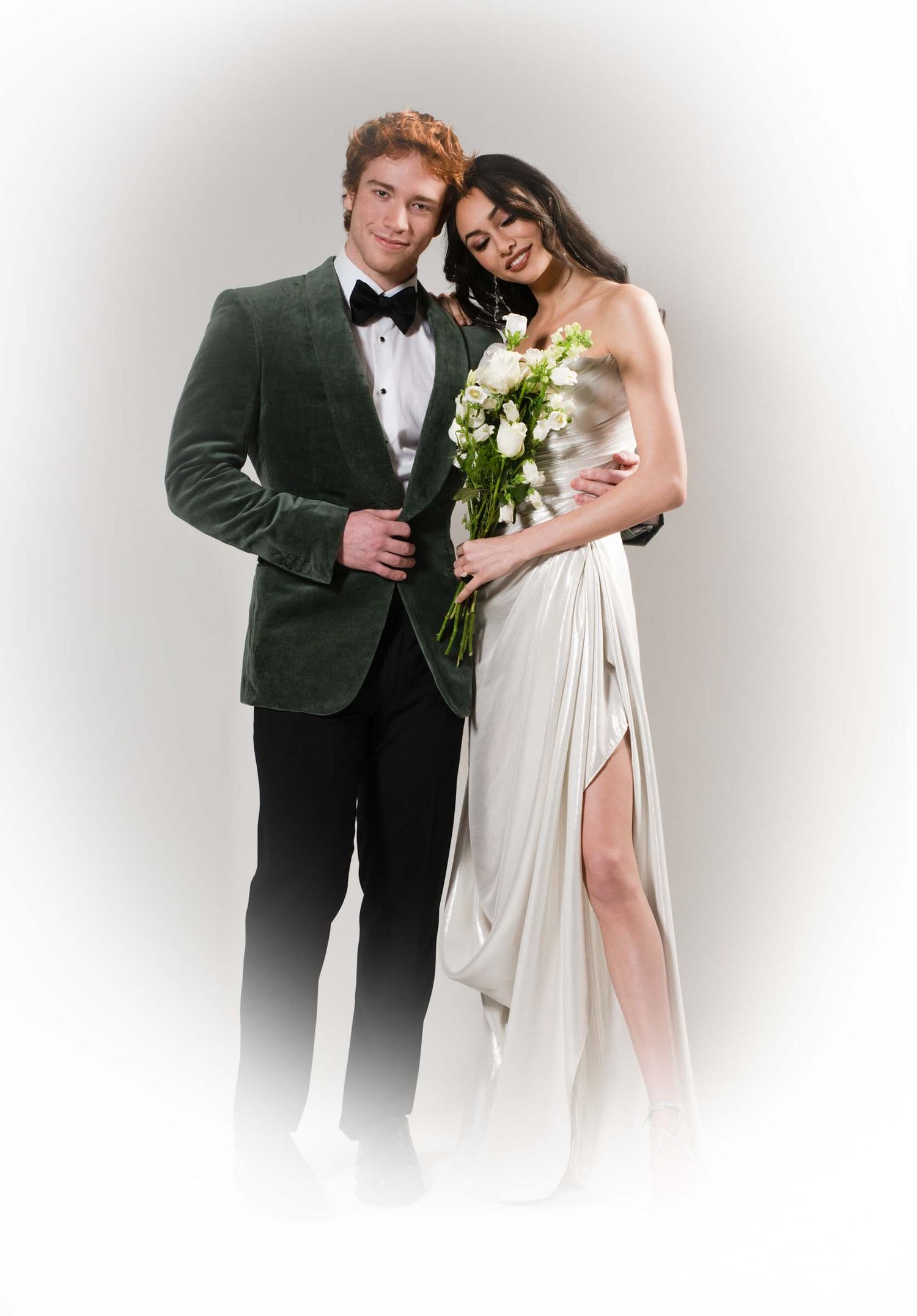 A couple in formal wedding attire poses together with white flowers against a light background.