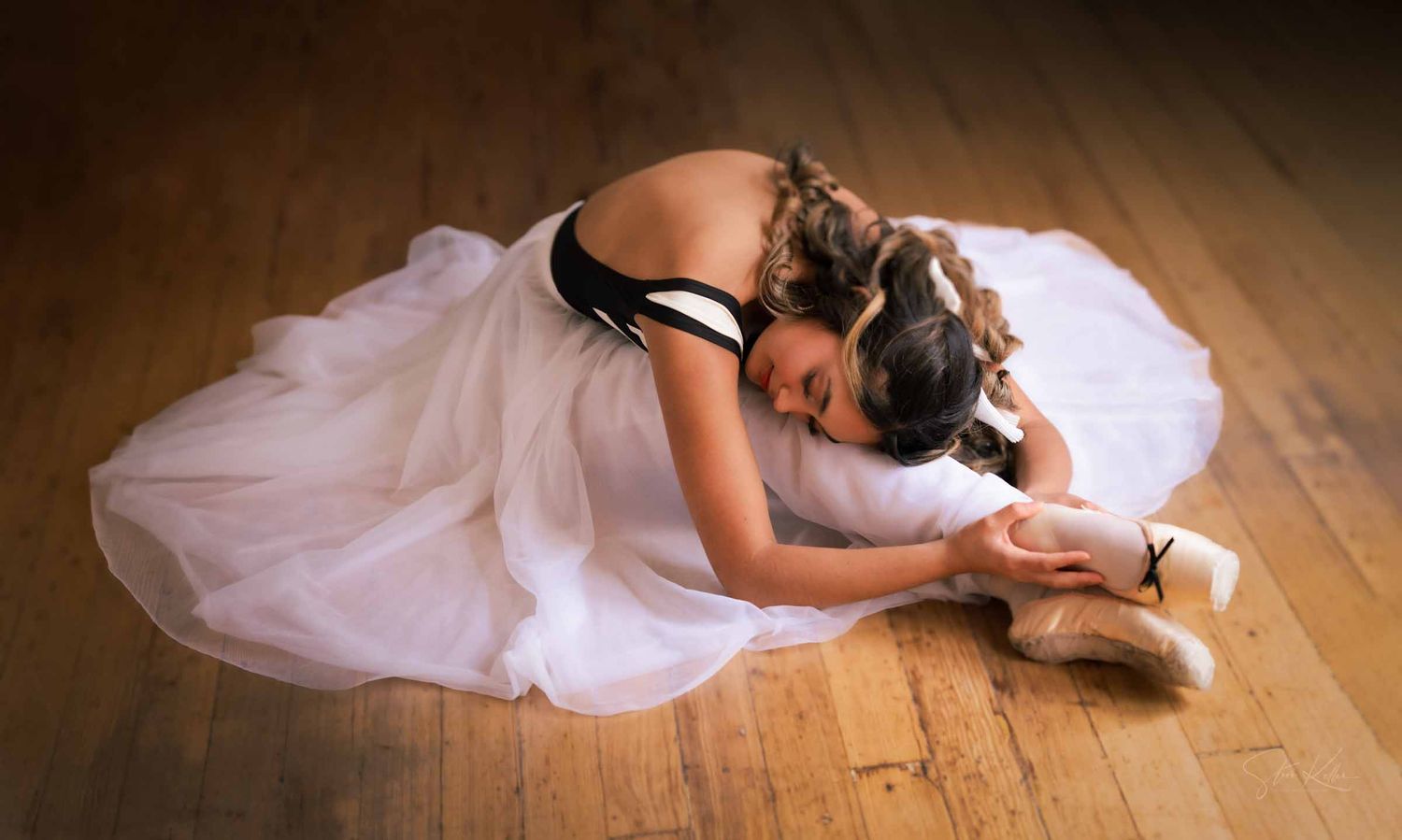 Ballet dancer in white tutu and pointe shoes performs graceful movements on wooden floor in artistic sequence.
