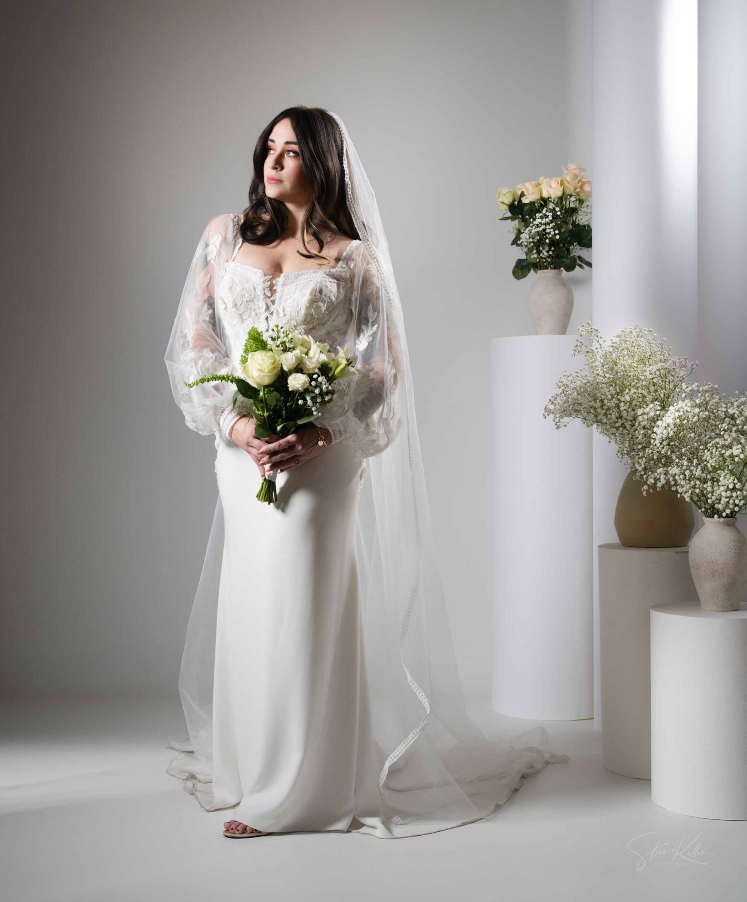 Minimalist bridal session in white studio with elegant wedding dress, baby's breath arrangements, and ceramic vases.