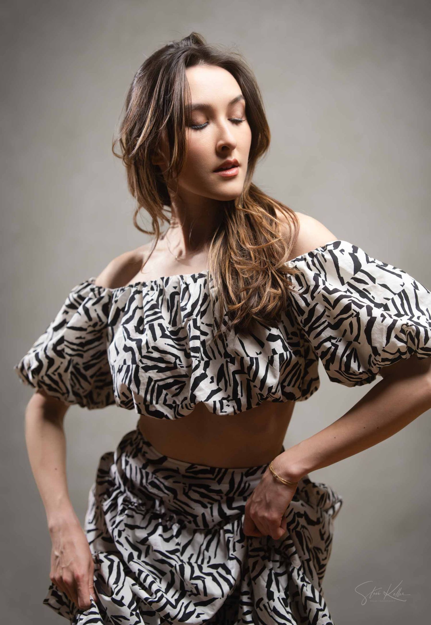 Fashion model wearing black and white zebra print dress with puff sleeves poses dynamically against gray backdrop.