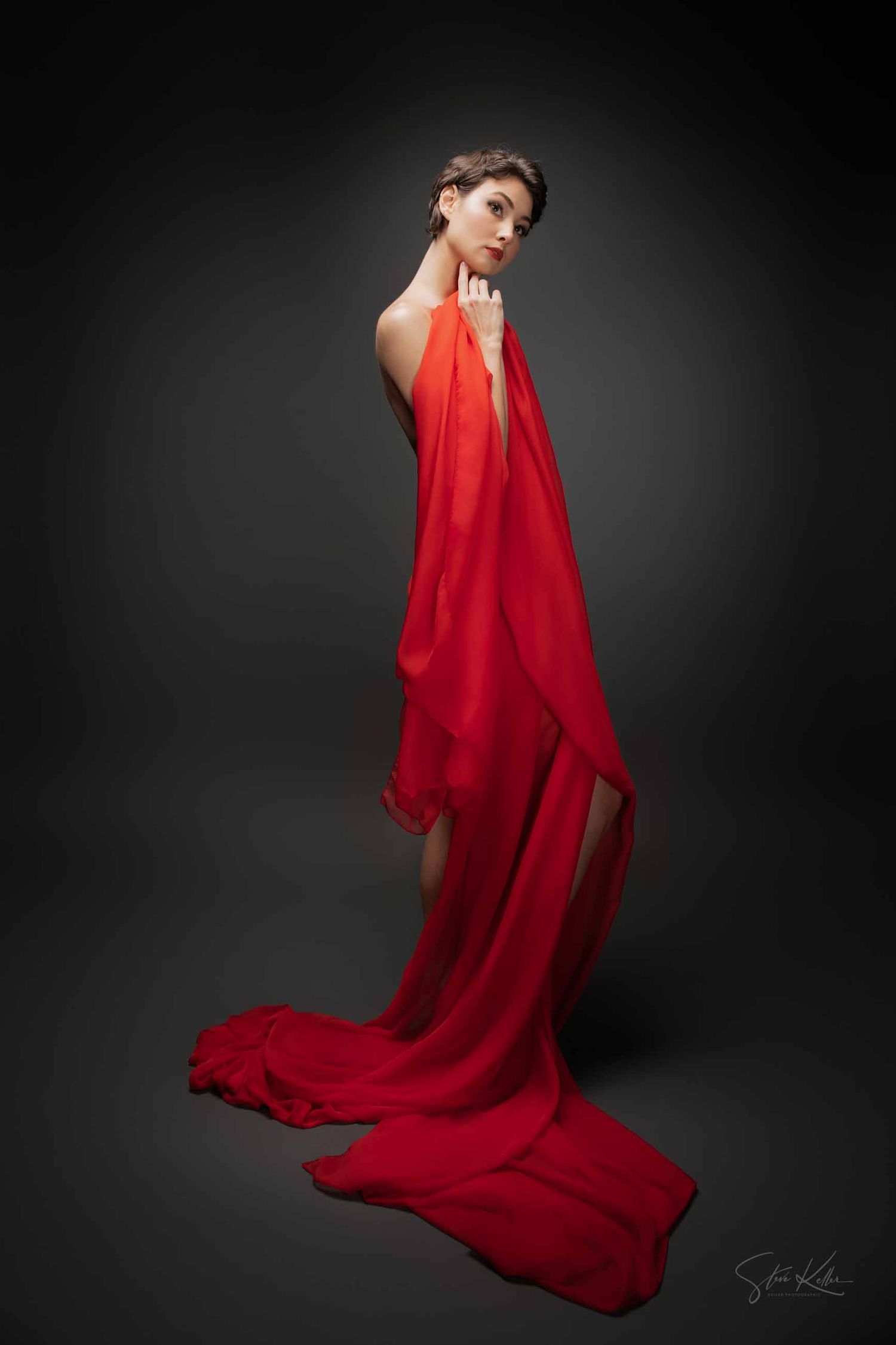 A figure in a flowing red dress poses dramatically against a dark background in a fashion photography series.