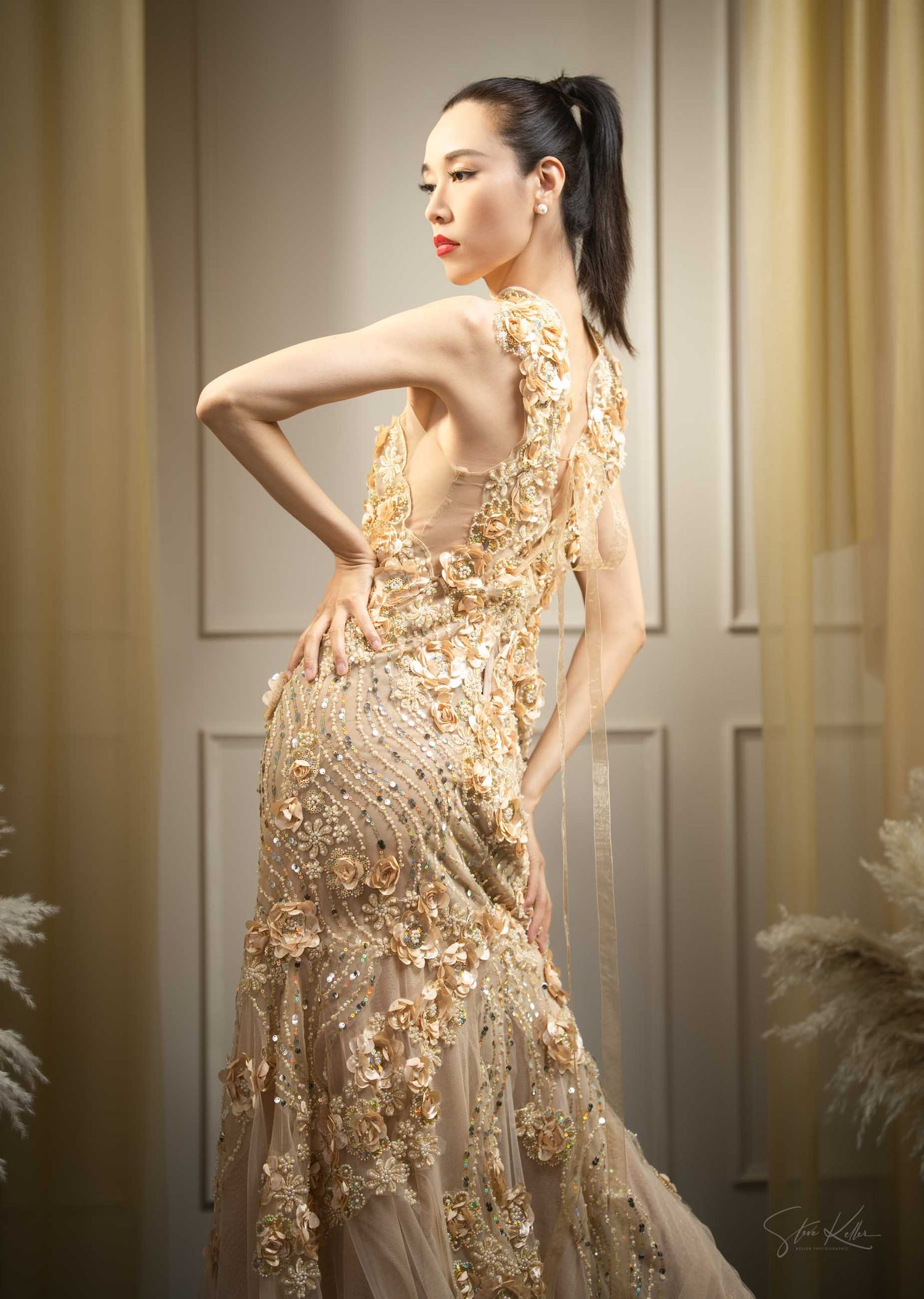 Ethereal evening gown in champagne with delicate floral embellishments and sheer overlay creates dramatic movement.