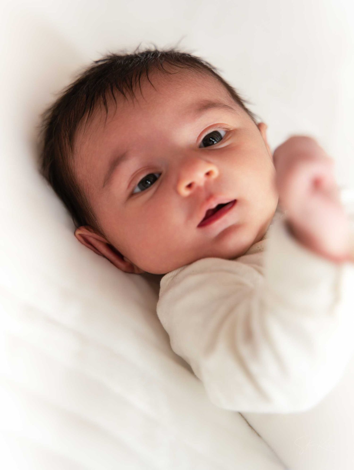Three close-up shots of a newborn baby in white clothing lying on white bedding.