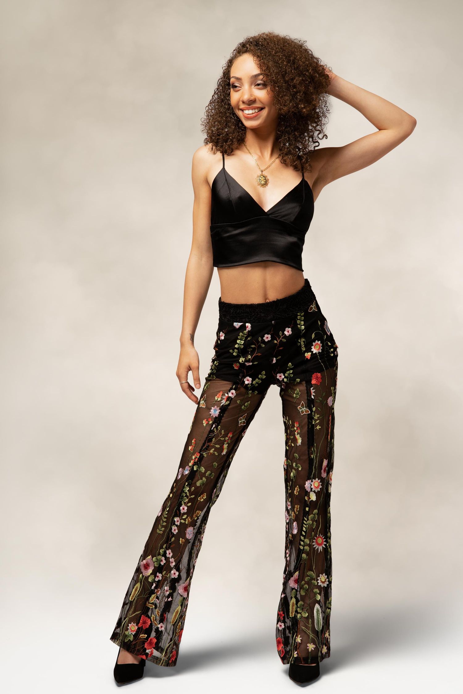 Fashion model poses in sheer black floral palazzo pants and crop top against neutral background.