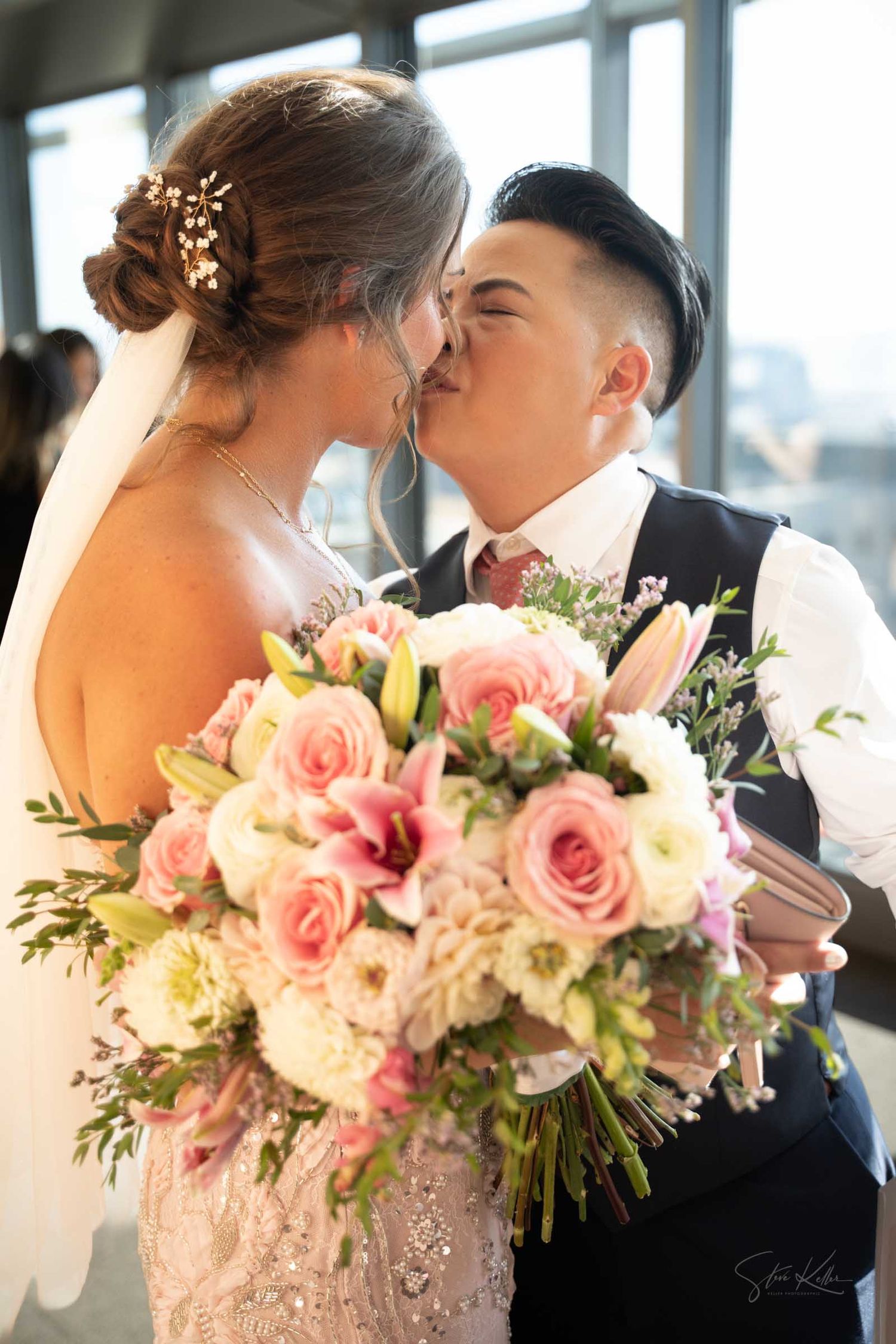 Newlyweds share a tender kiss as bride holds a lush pink and white rose wedding bouquet.
