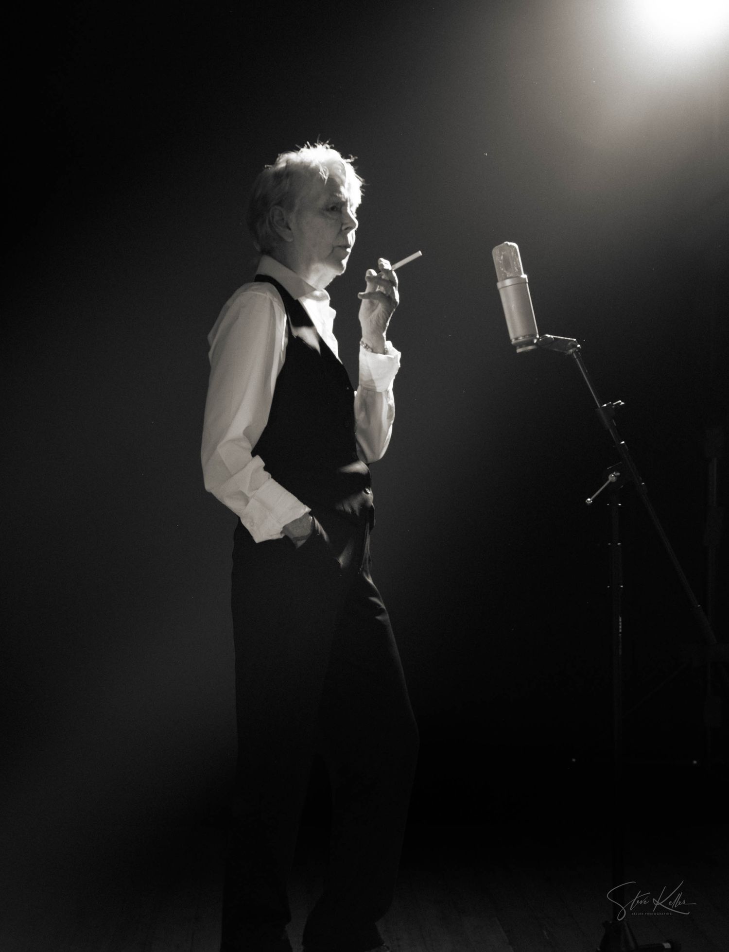 Dramatic black and white silhouettes show someone performing on stage with strong backlighting and theatrical smoke.