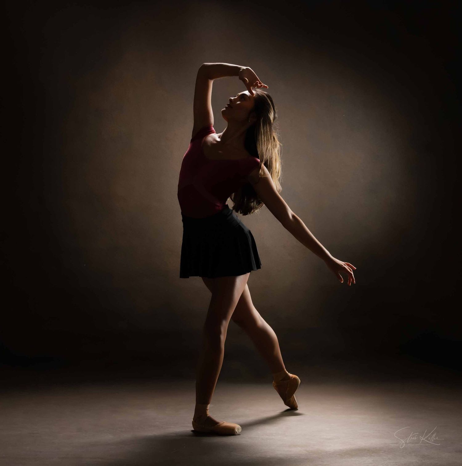 Silhouetted dancer in dramatic lighting strikes elegant pose with raised arm.