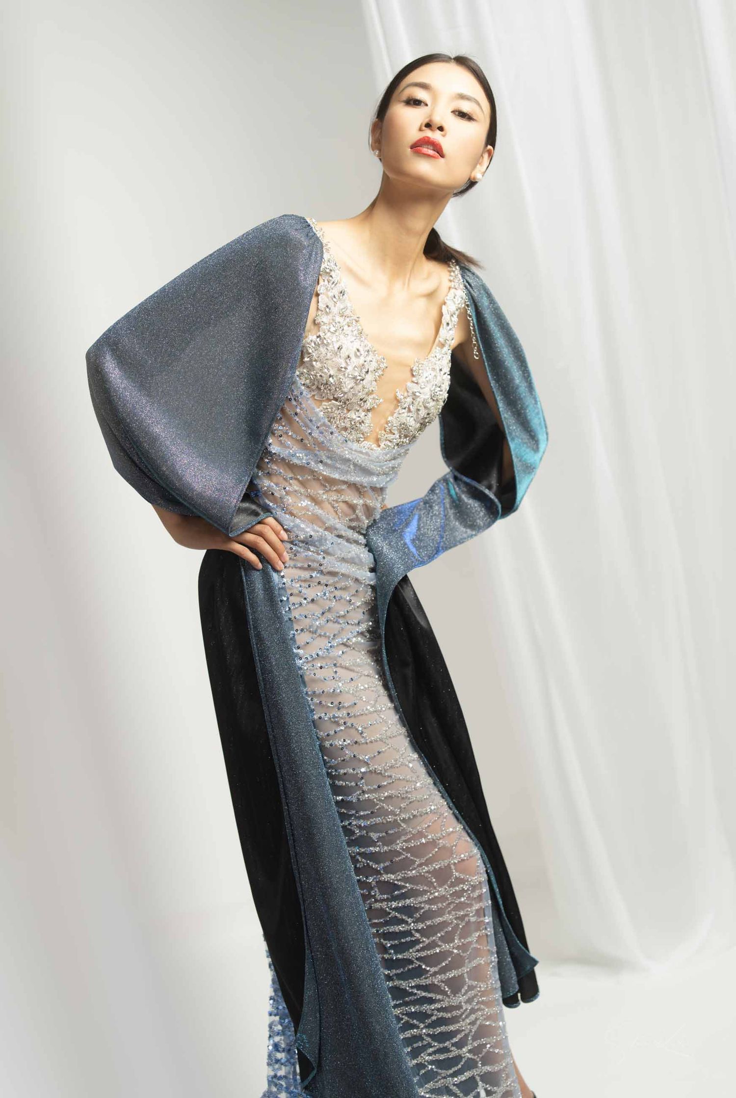 Fashion model poses in a silver sequined evening gown with dramatic dark balloon sleeves against a white backdrop.