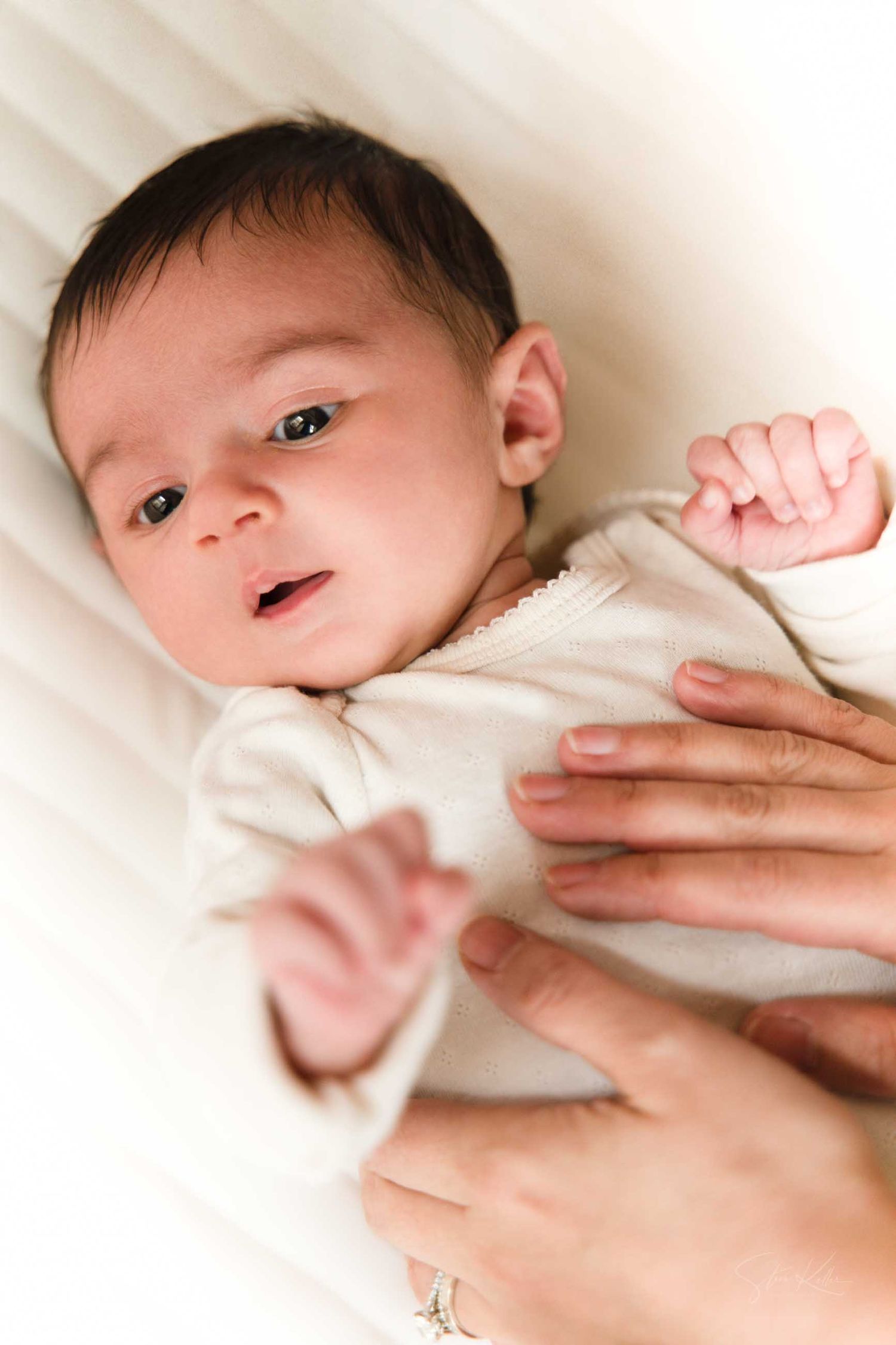 A series of photos showing a newborn baby in white clothing being gently held by caring hands.