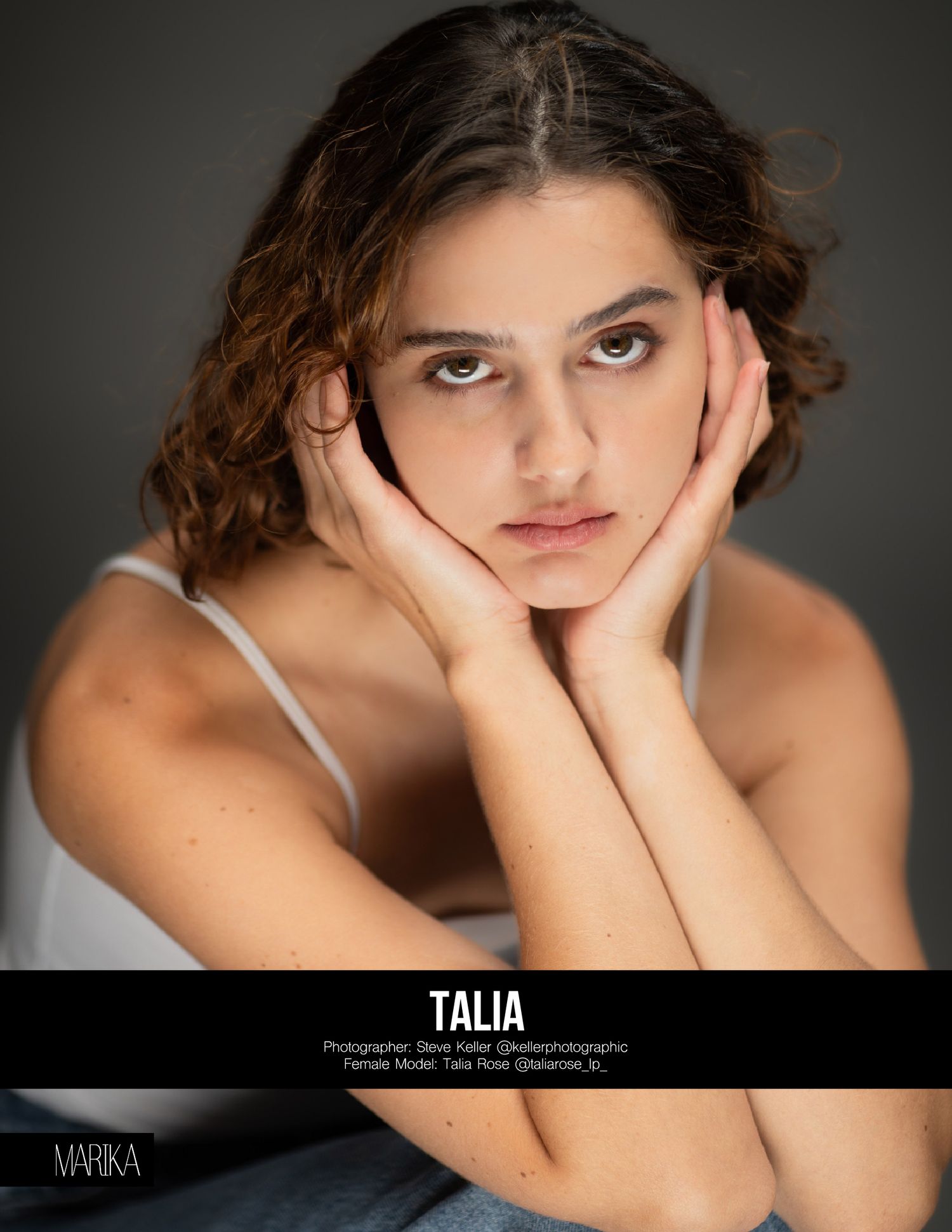 A professional portrait photograph shows a woman in white top resting her face between both hands against a dark background.
