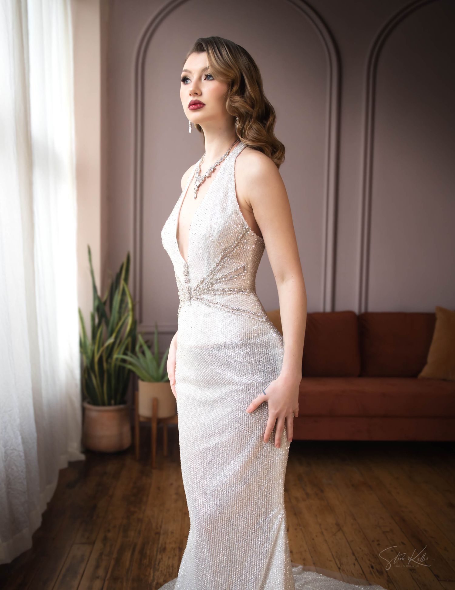 Elegant lace wedding dress with plunging neckline and fitted silhouette photographed in soft interior lighting.