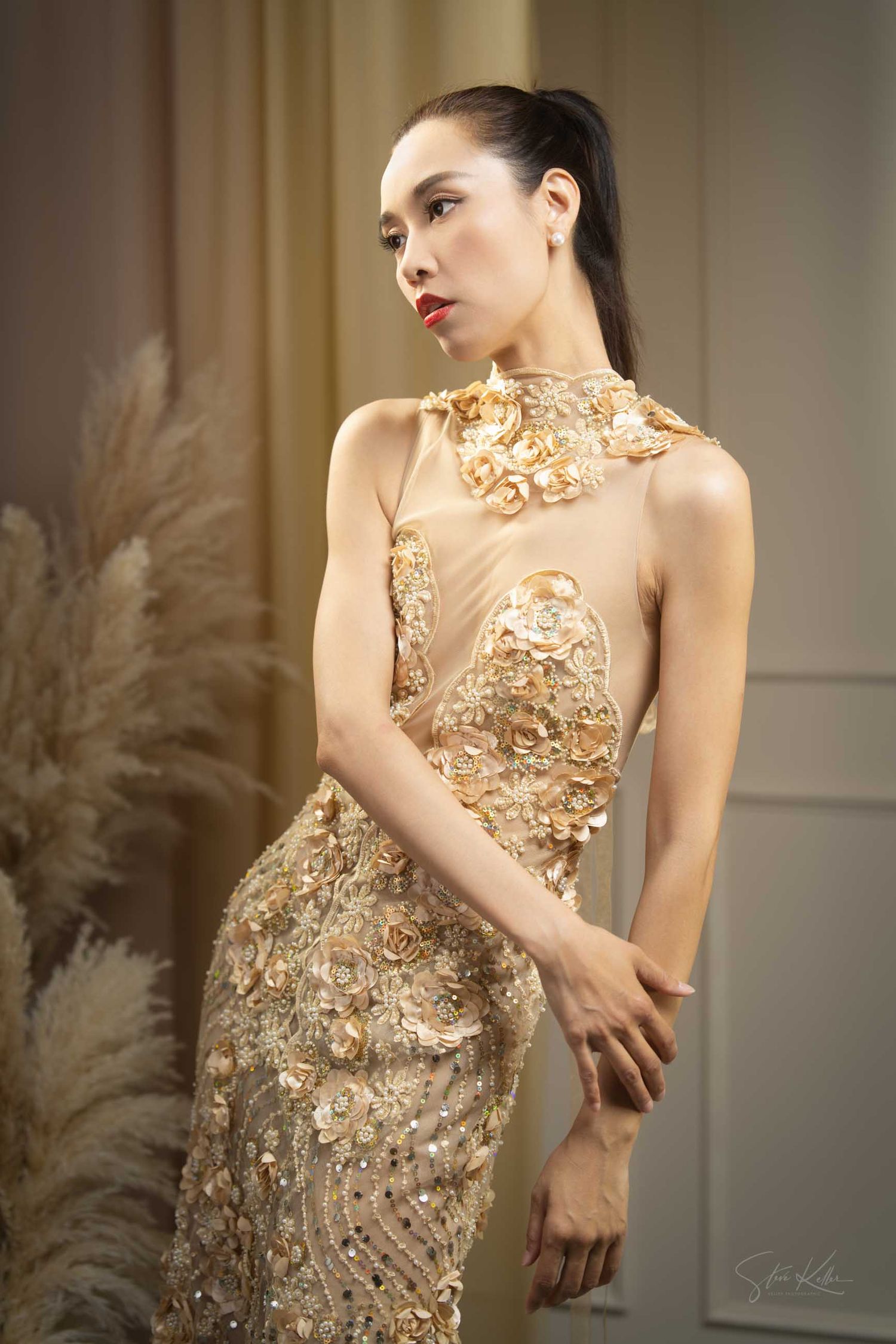 Elegant gold sequined evening gown with intricate beading and sheer details photographed in a studio setting.