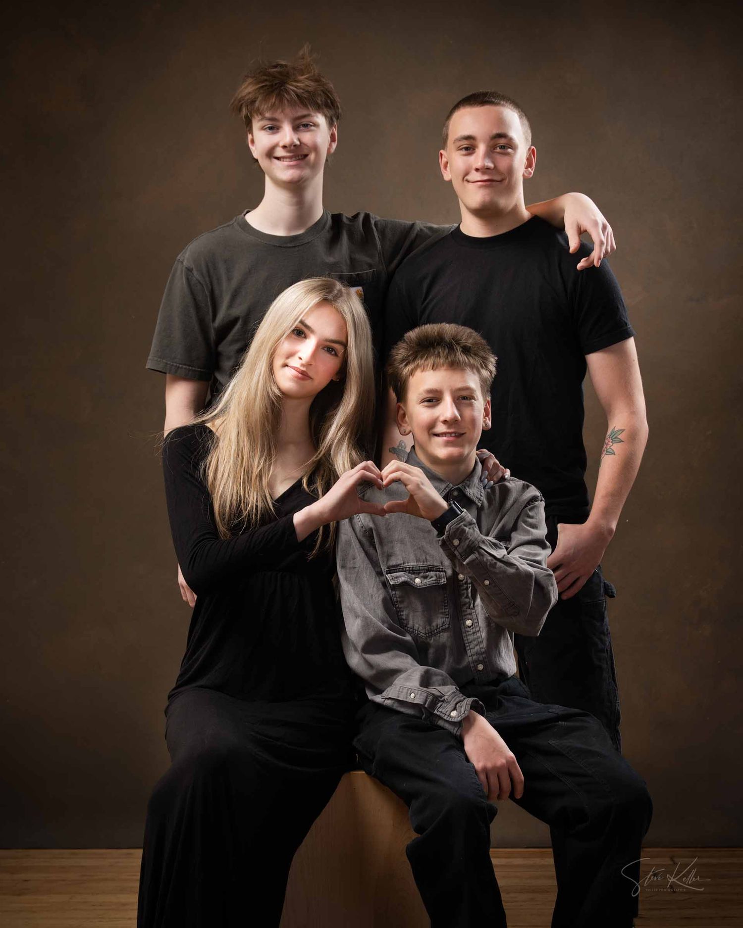 A group wearing black shirts poses together against a dark brown backdrop in a studio portrait setting.