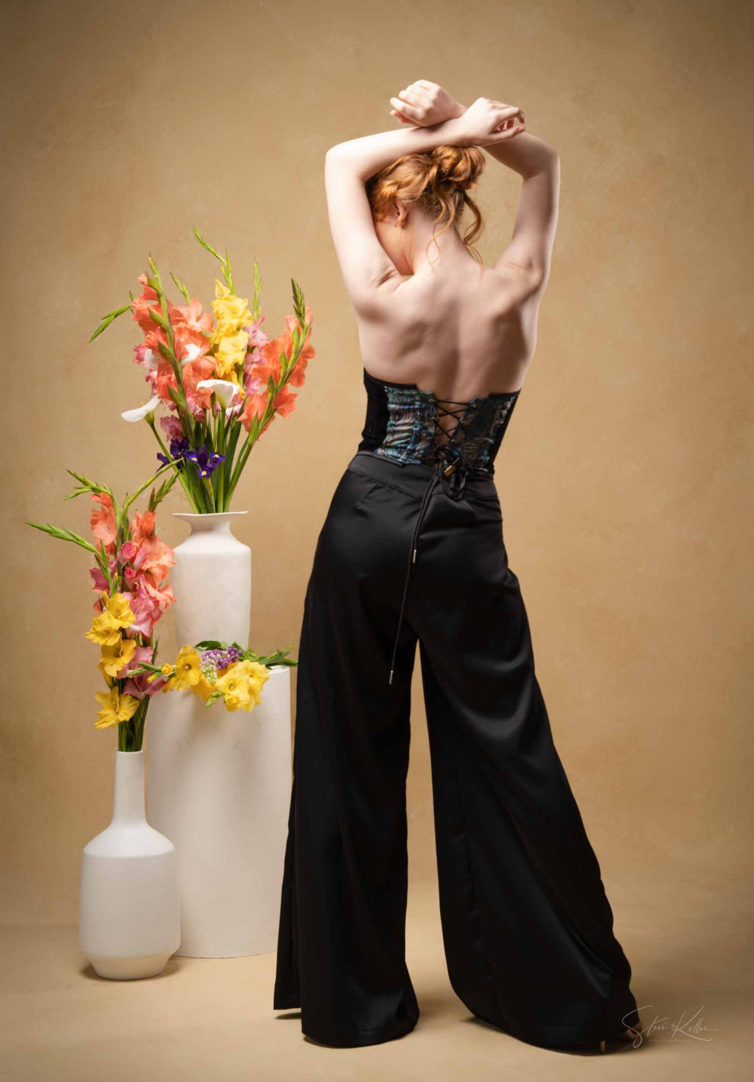 Artistic fashion series with black pants against beige backdrop, styled with white vases and vibrant flowers.