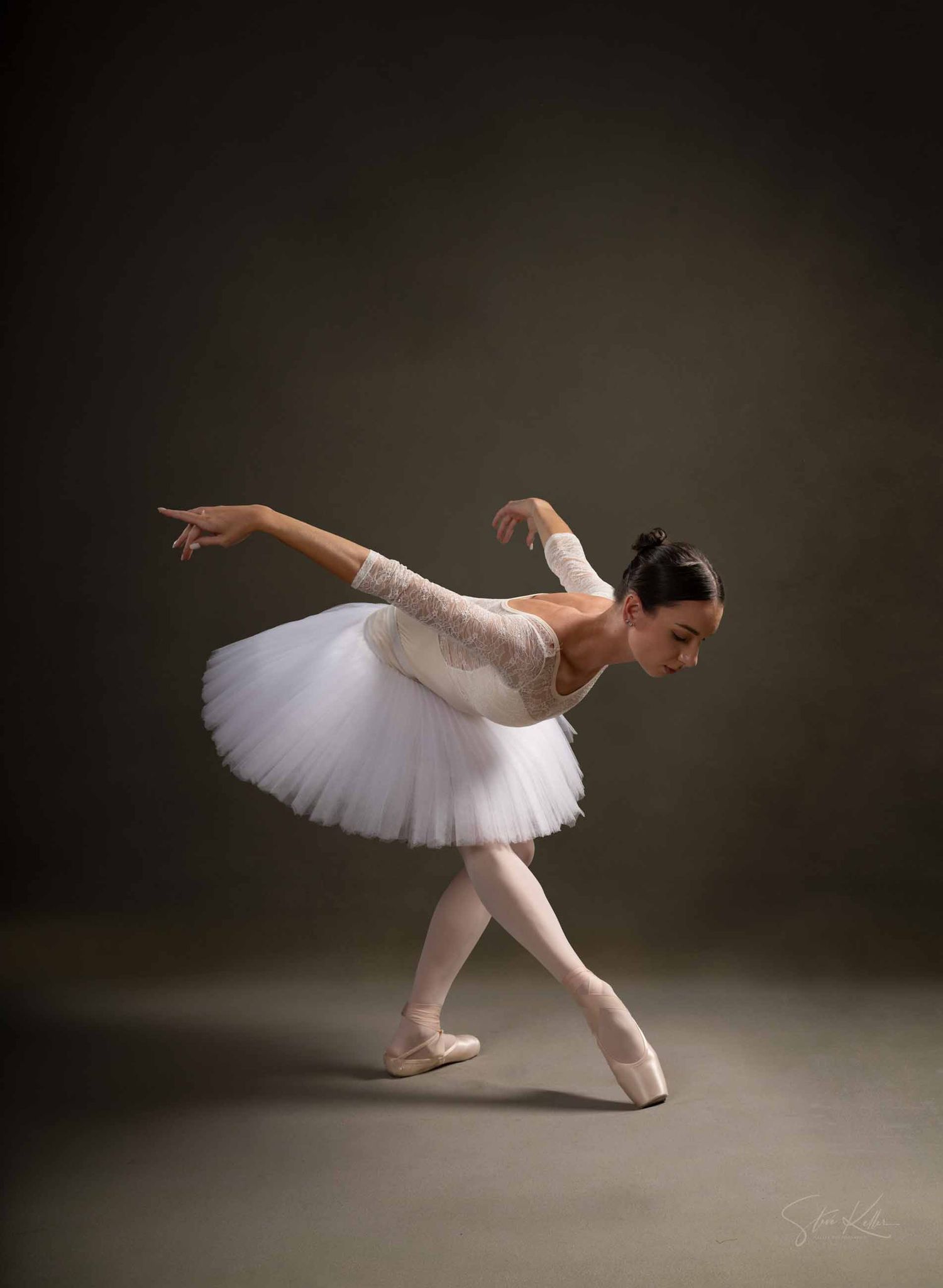 A ballet dancer in a white tutu performs a graceful sequence of movements in a dramatic studio setting.