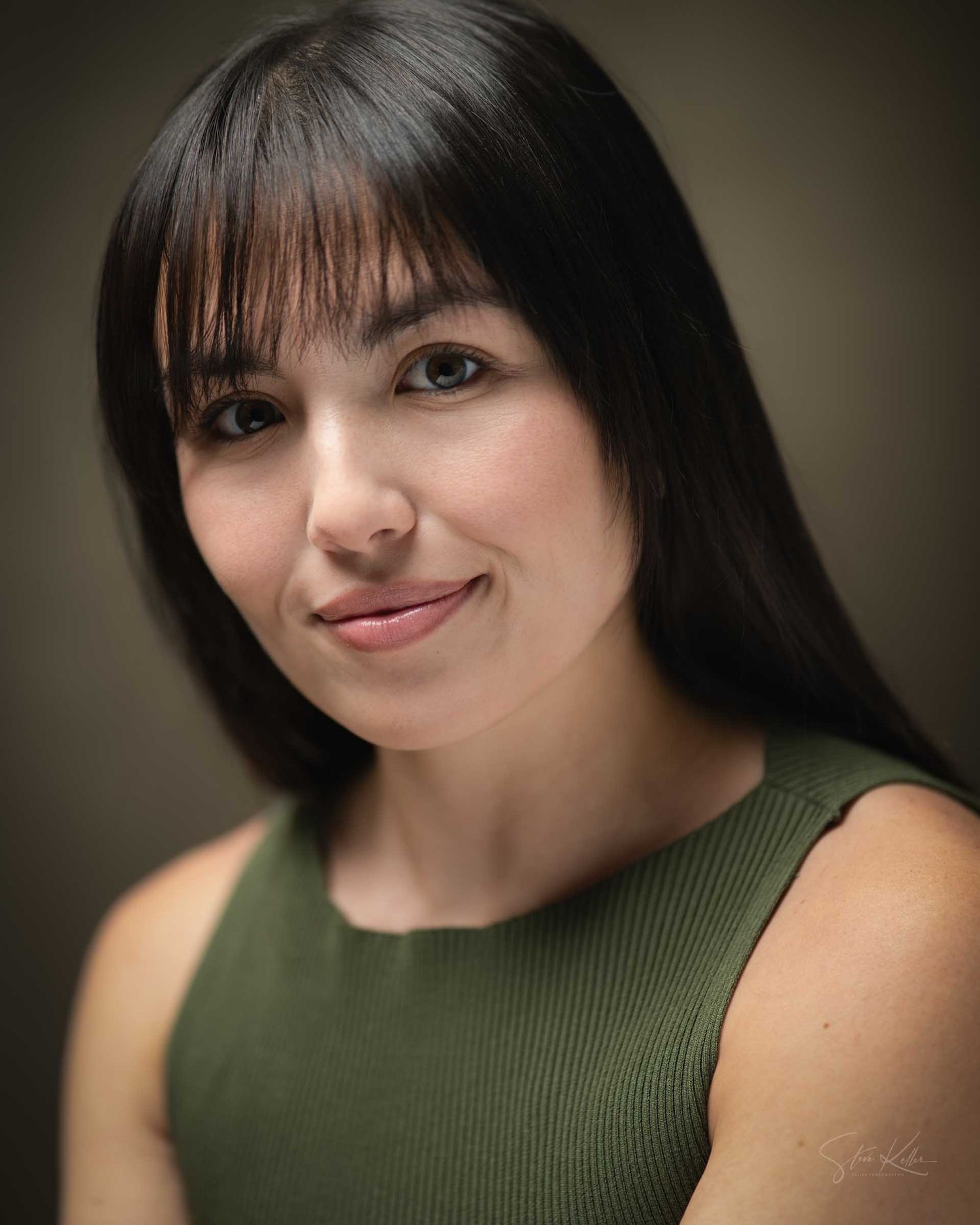A young woman with dark hair and bangs smiles confidently in a professional headshot, wearing a green sleeveless top.