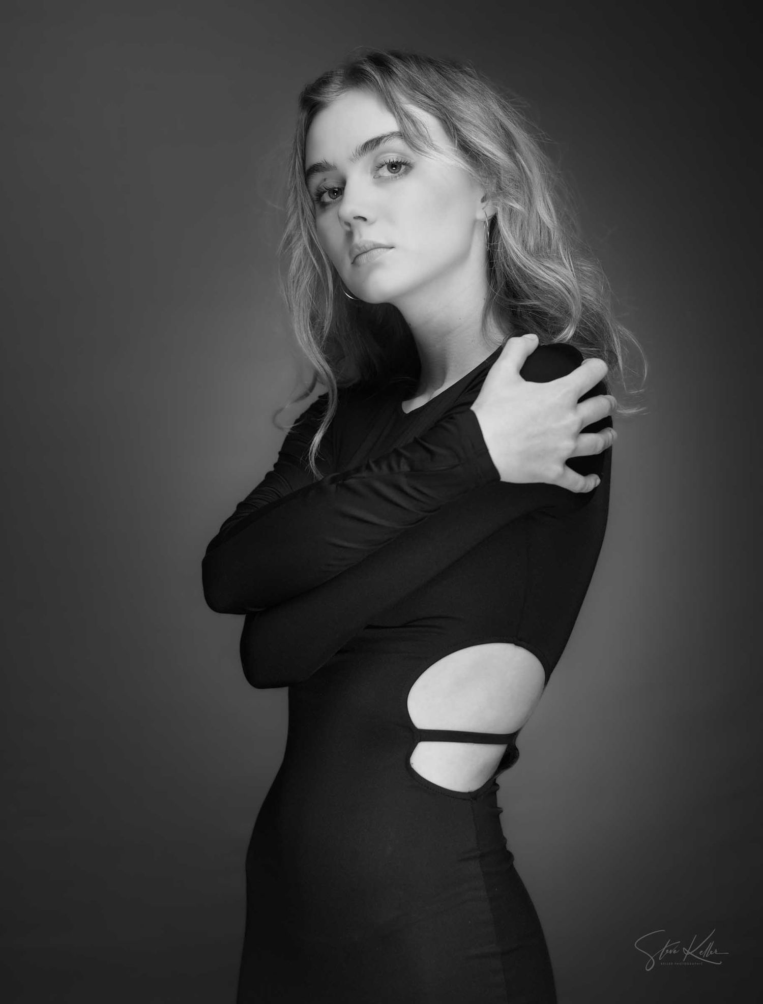 Artistic black and white portrait of a woman in a black dress with cutout details against a dark background.