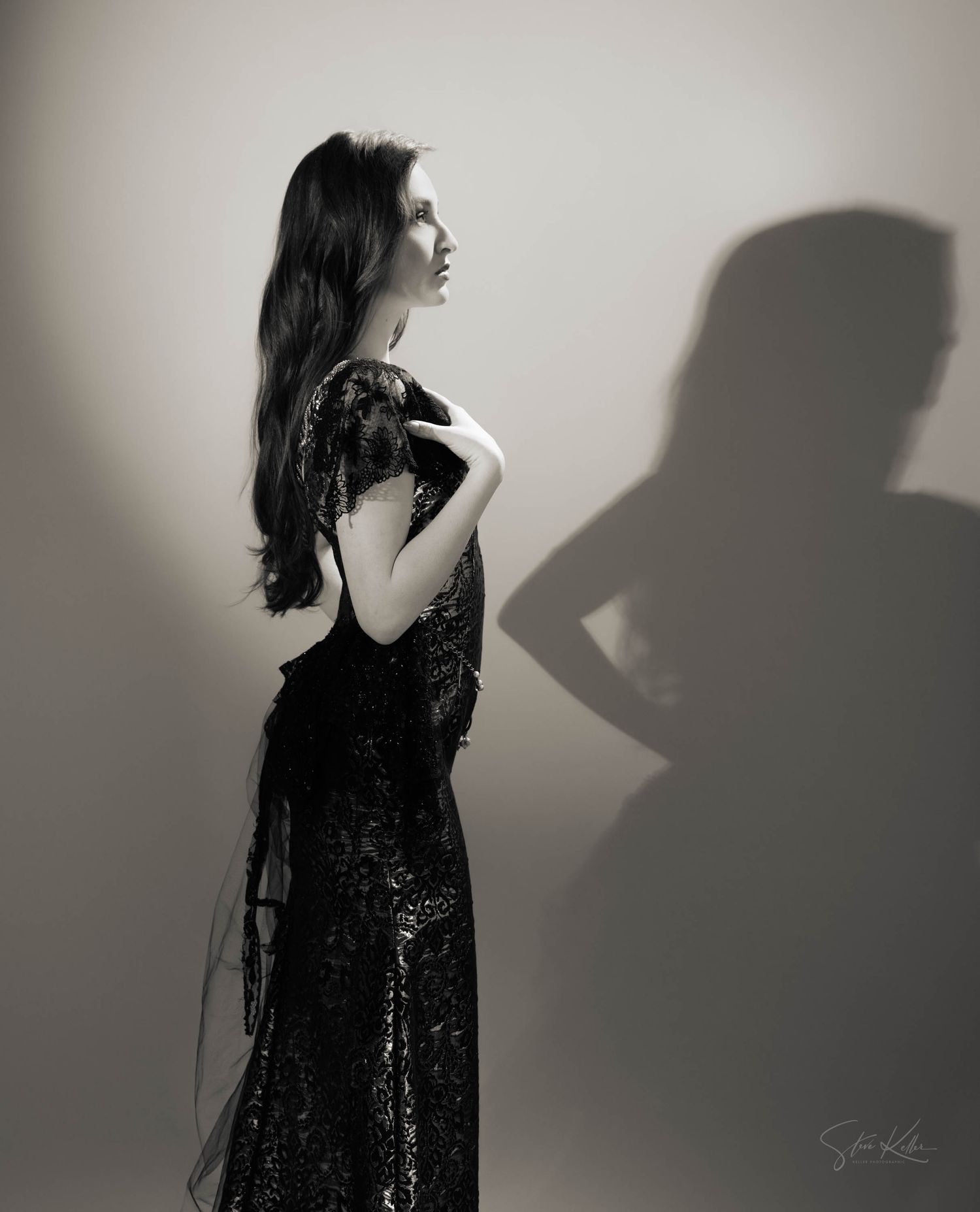 Dramatic black and white portrait of fashion model in sequined gown casting shadow against light background in film noir style.