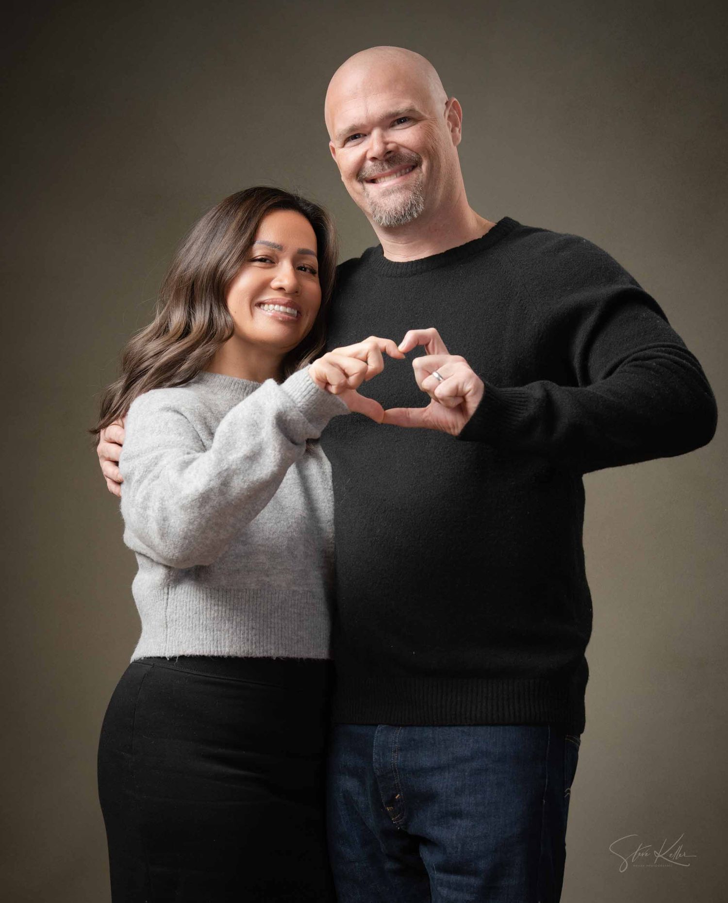 A couple in black and gray sweaters embrace and laugh together in a series of candid studio portraits.