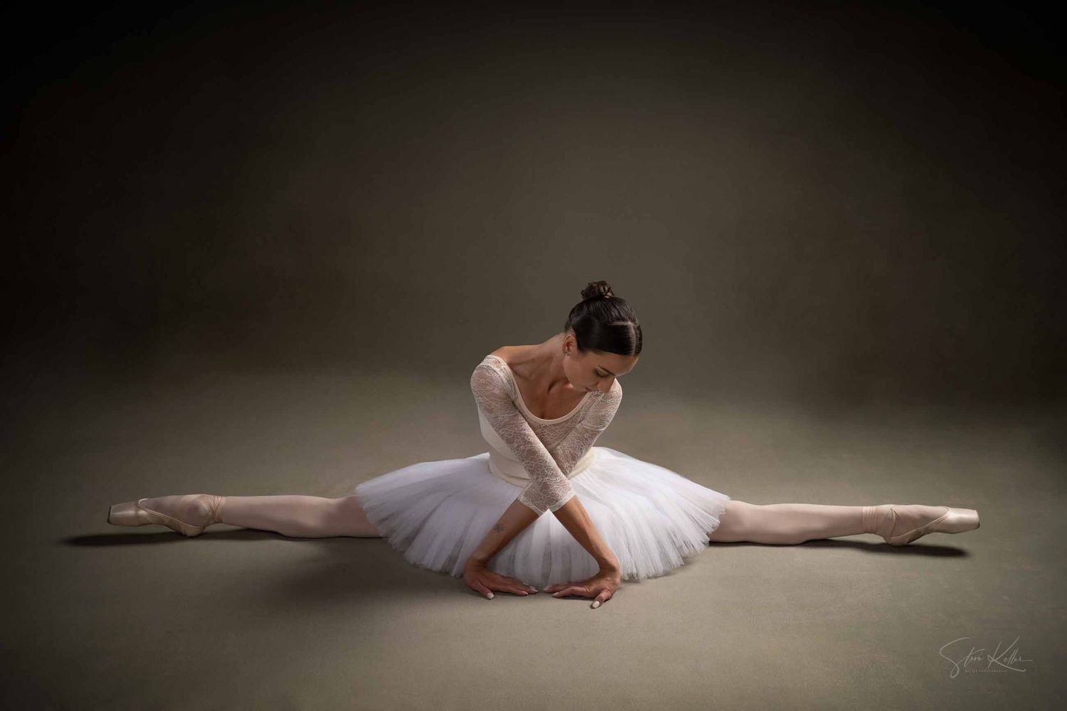 A graceful ballet dancer in white tutu performs a dramatic split pose against a dark background.