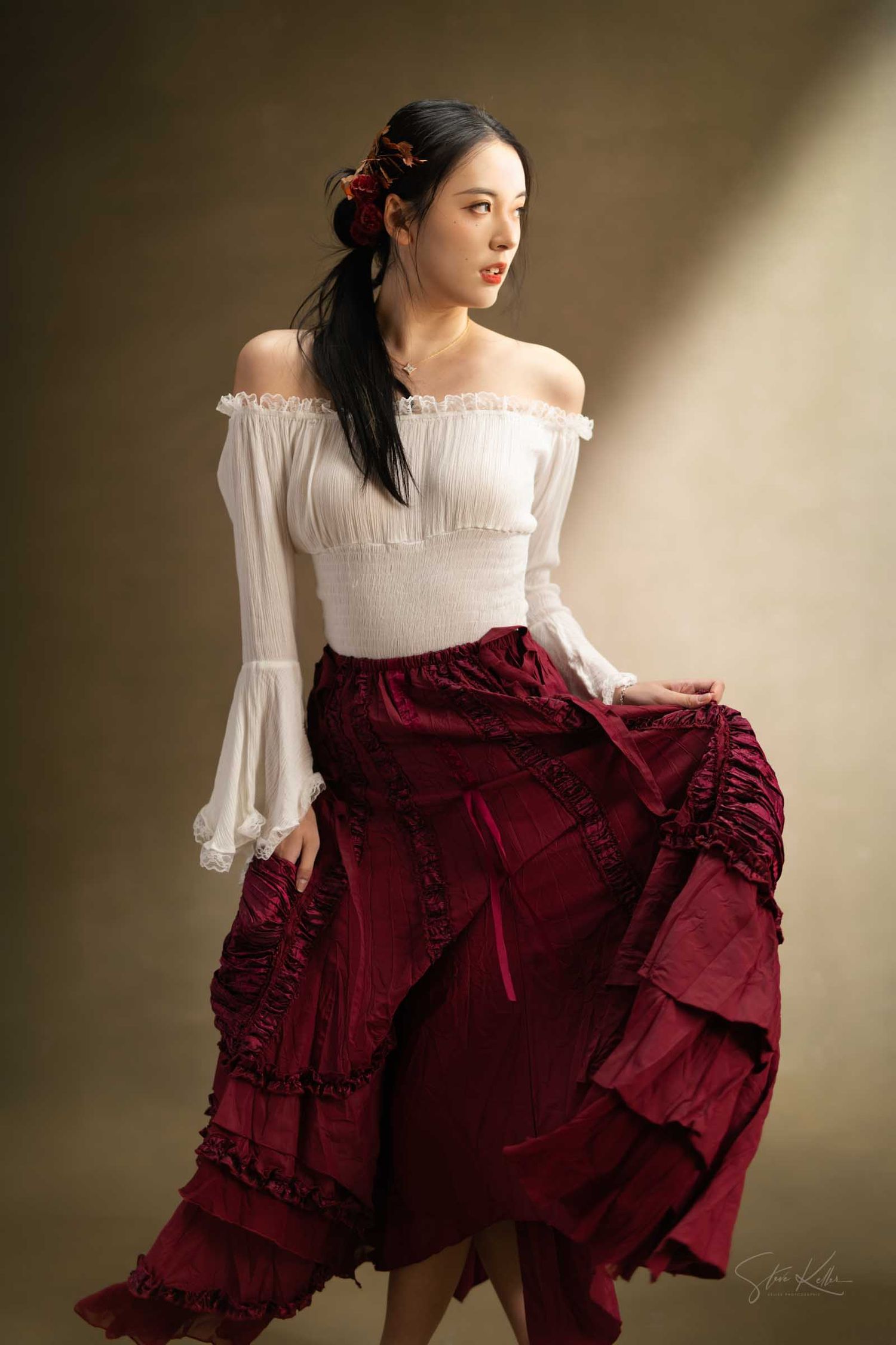 A woman wearing a white peasant top demonstrates the dramatic flow of a deep burgundy tiered skirt in studio lighting.
