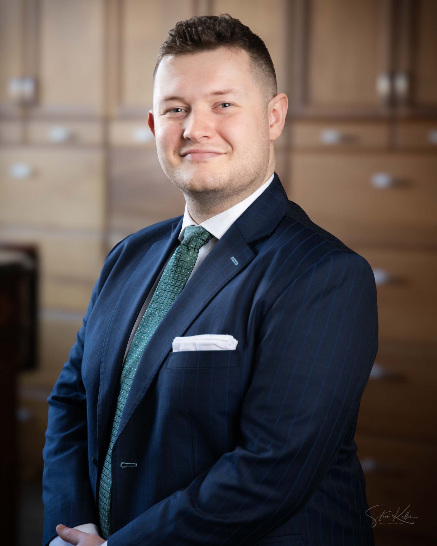 Professional man in navy suit and green tie smiling confidently in a formal portrait setting.