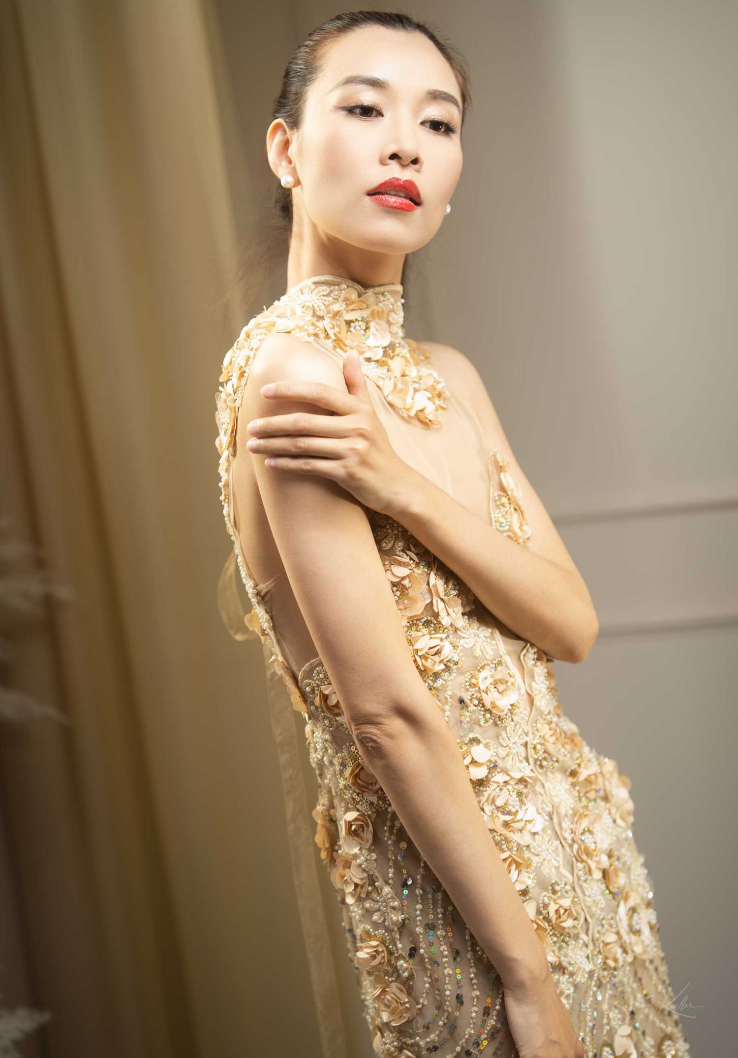 Fashion model poses in a glamorous gold sequined dress against a neutral background.
