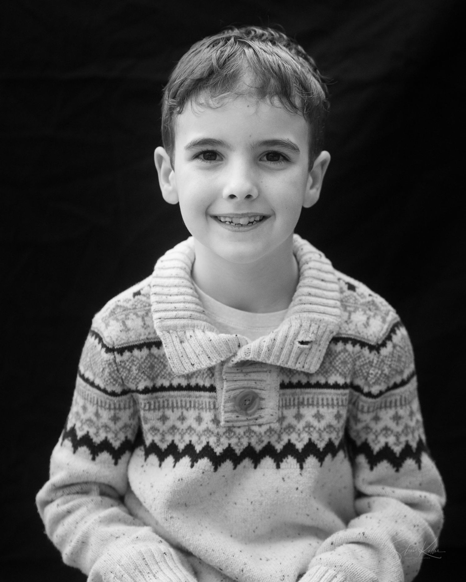 Child wearing a patterned knit sweater poses for a black and white portrait.