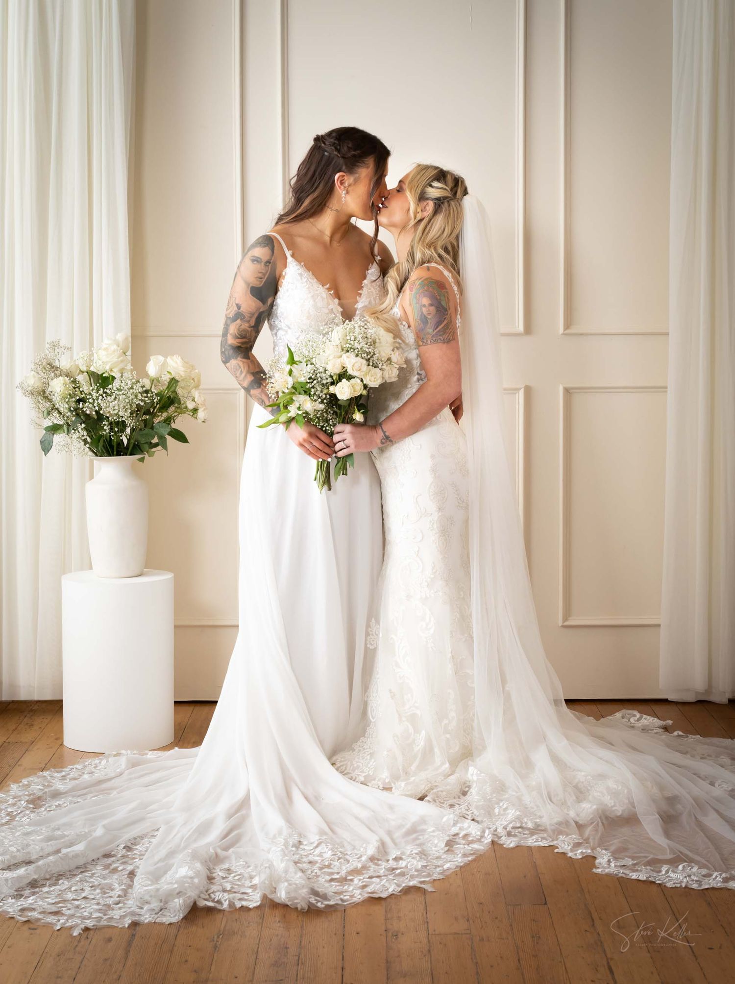 A stunning white wedding dress with lace details and long train photographed against a light colored wall.
