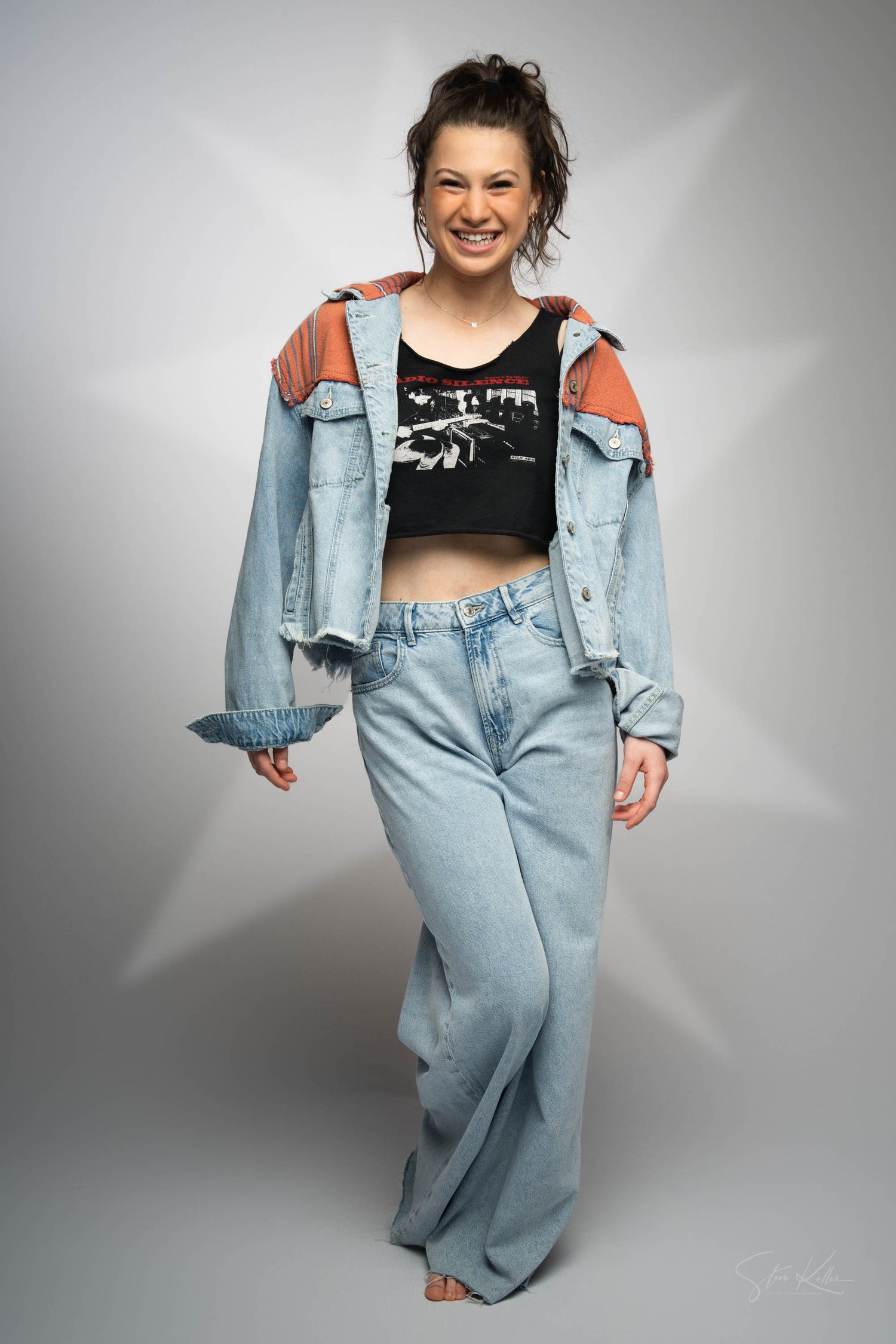 Smiling fashion model wearing oversized denim jacket, black crop top and baggy mom jeans in casual 90s inspired fashion look.