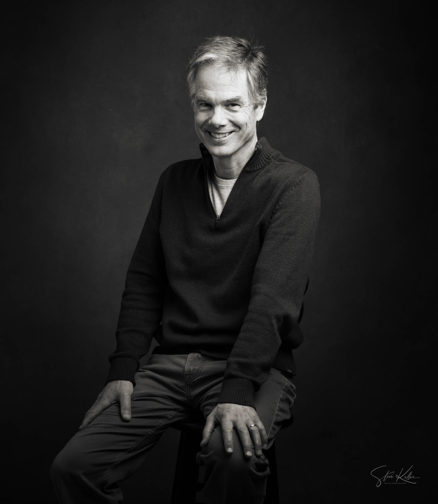 Professional headshot portrait against dark background with dramatic lighting.