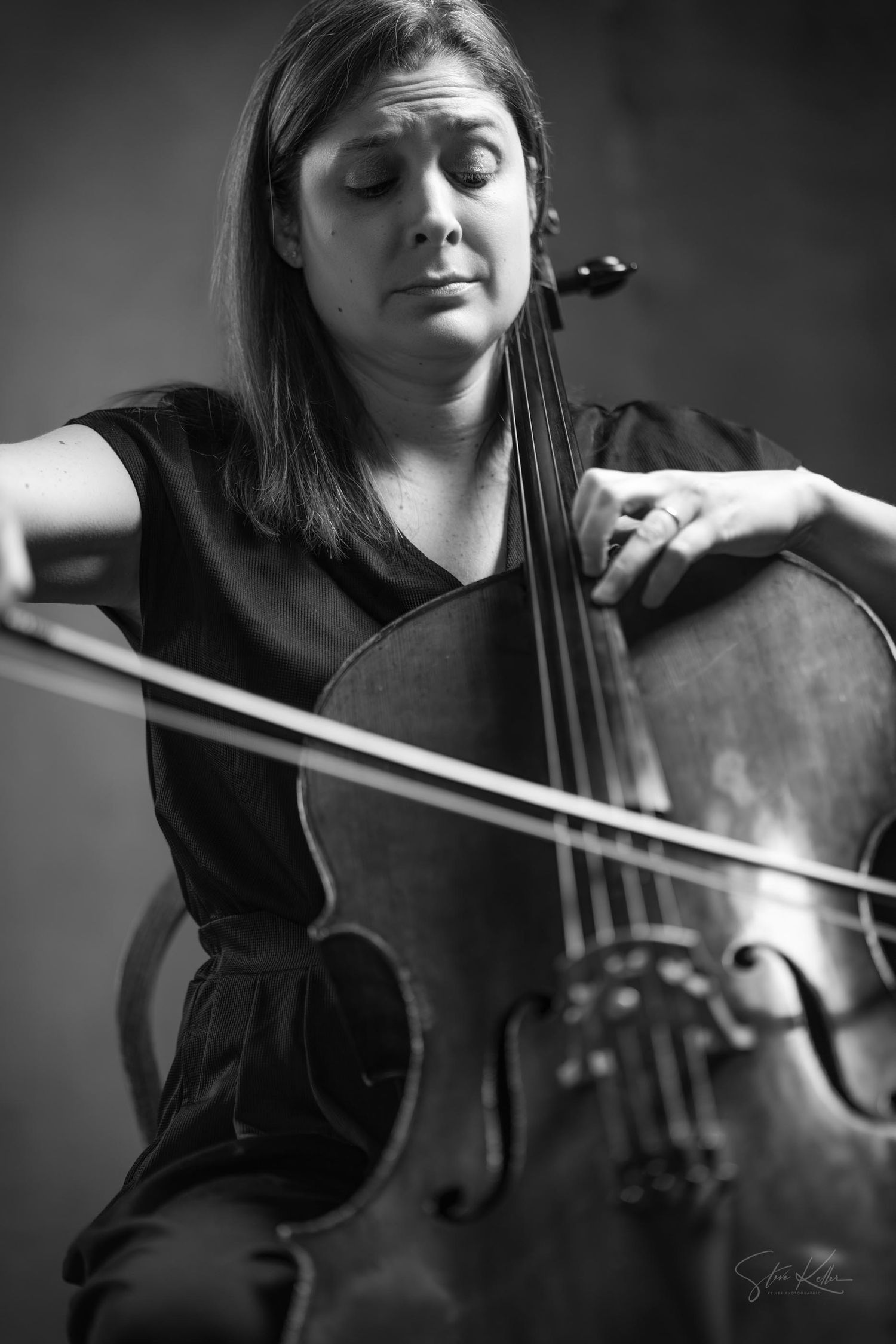 A black and white photograph of a cellist performing with eyes closed while playing their instrument.
