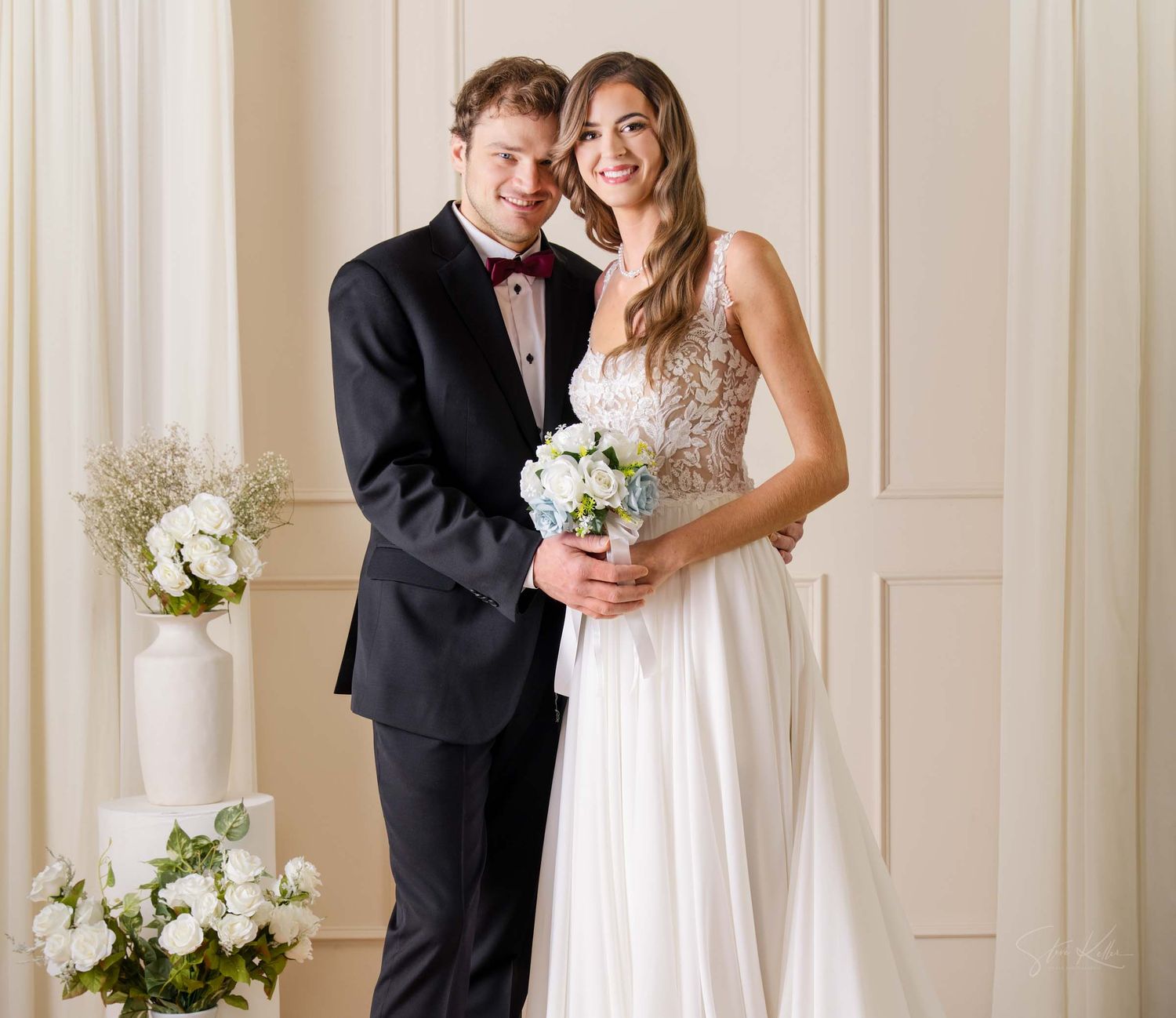 A bride and groom share a romantic moment in an elegant room with white paneled walls and white floral bouquets.