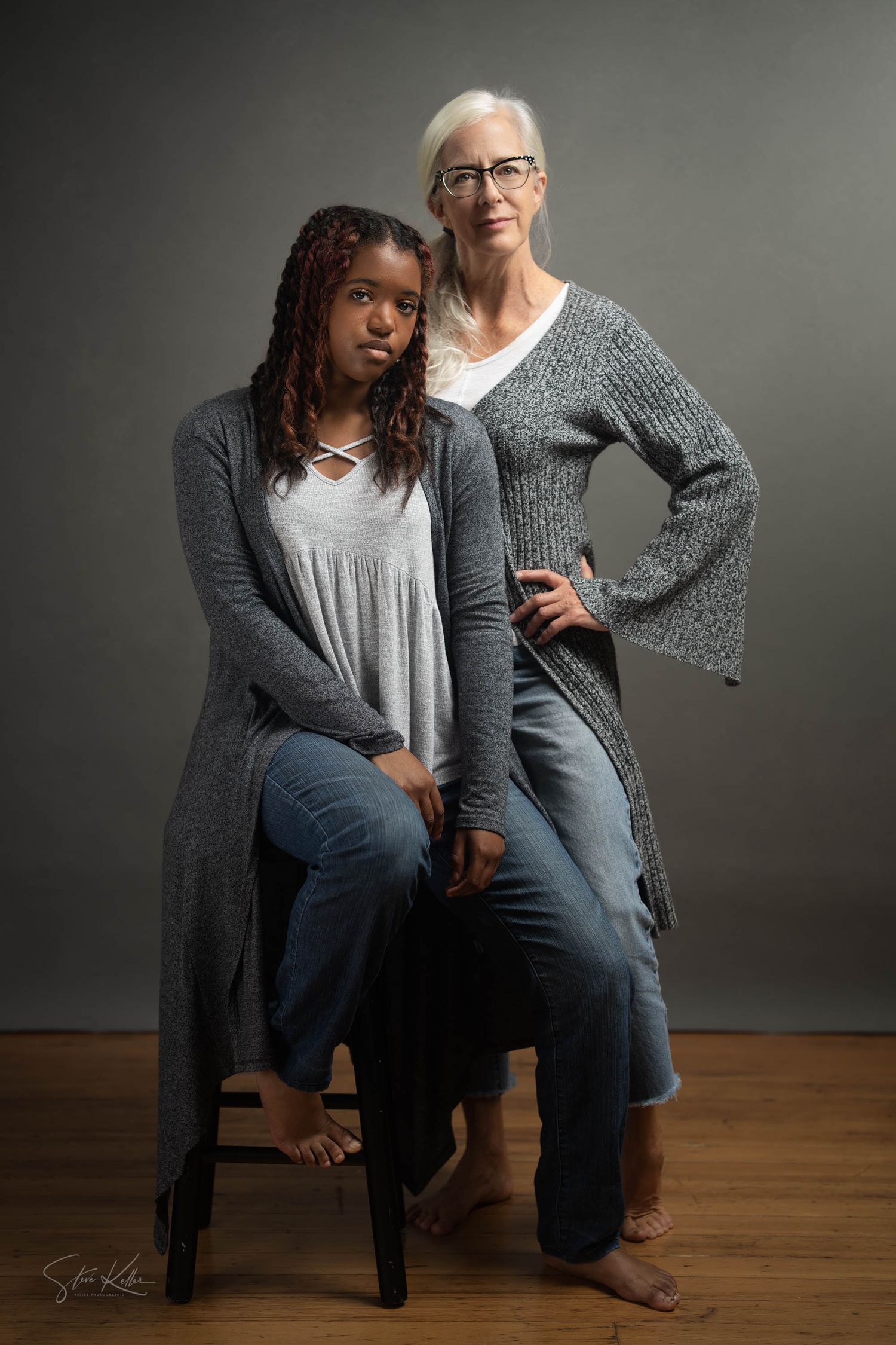 Portrait of two people in gray sweaters posing confidently in studio setting.