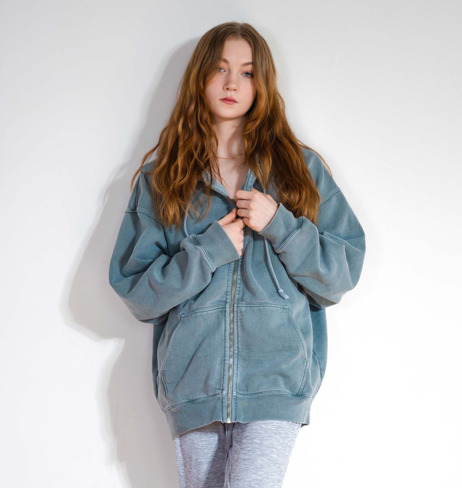 Model in oversized blue denim jacket poses against white wall in fashion photoshoot series.
