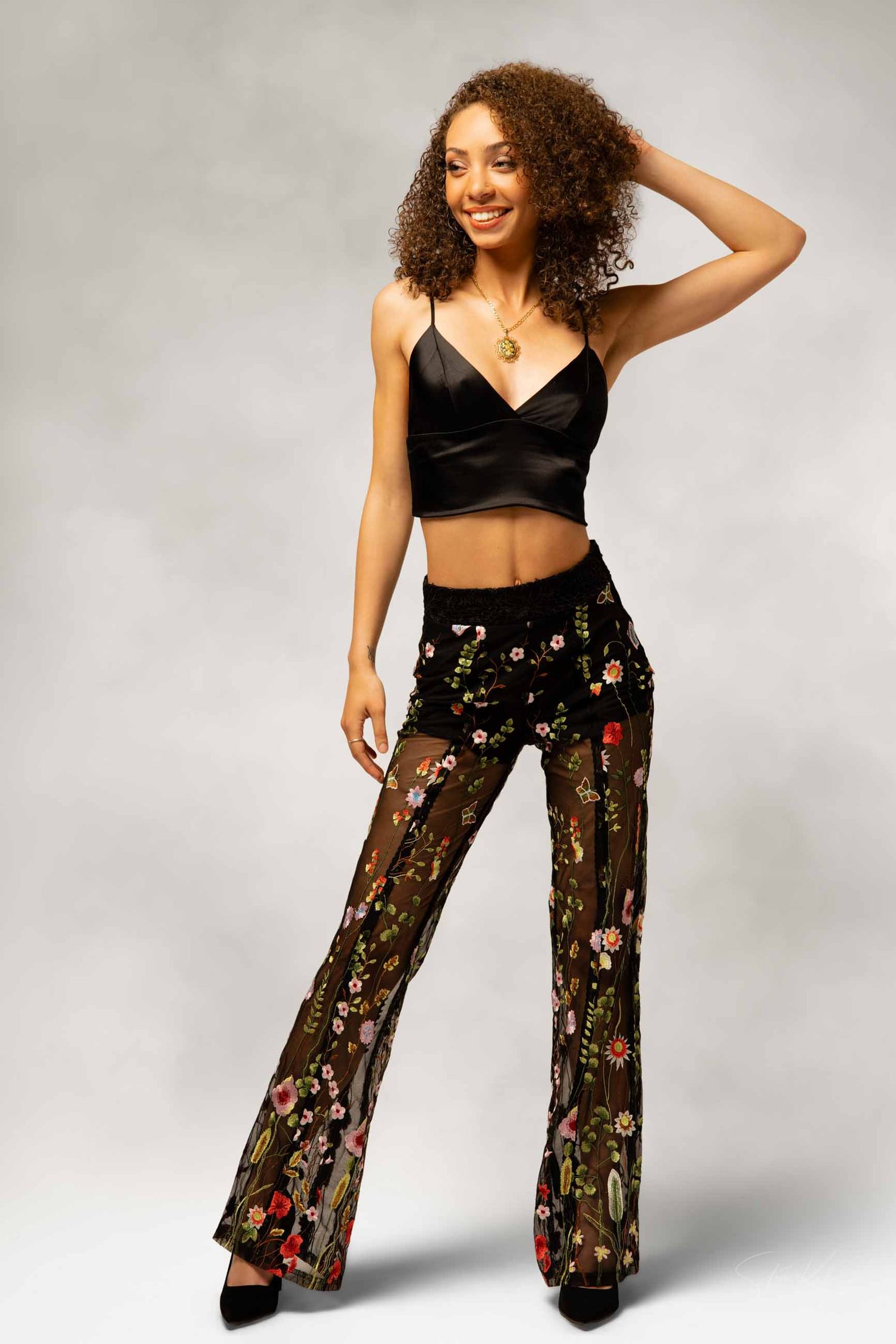 Model poses in black crop top and sheer floral palazzo pants against white background showing different angles and poses.
