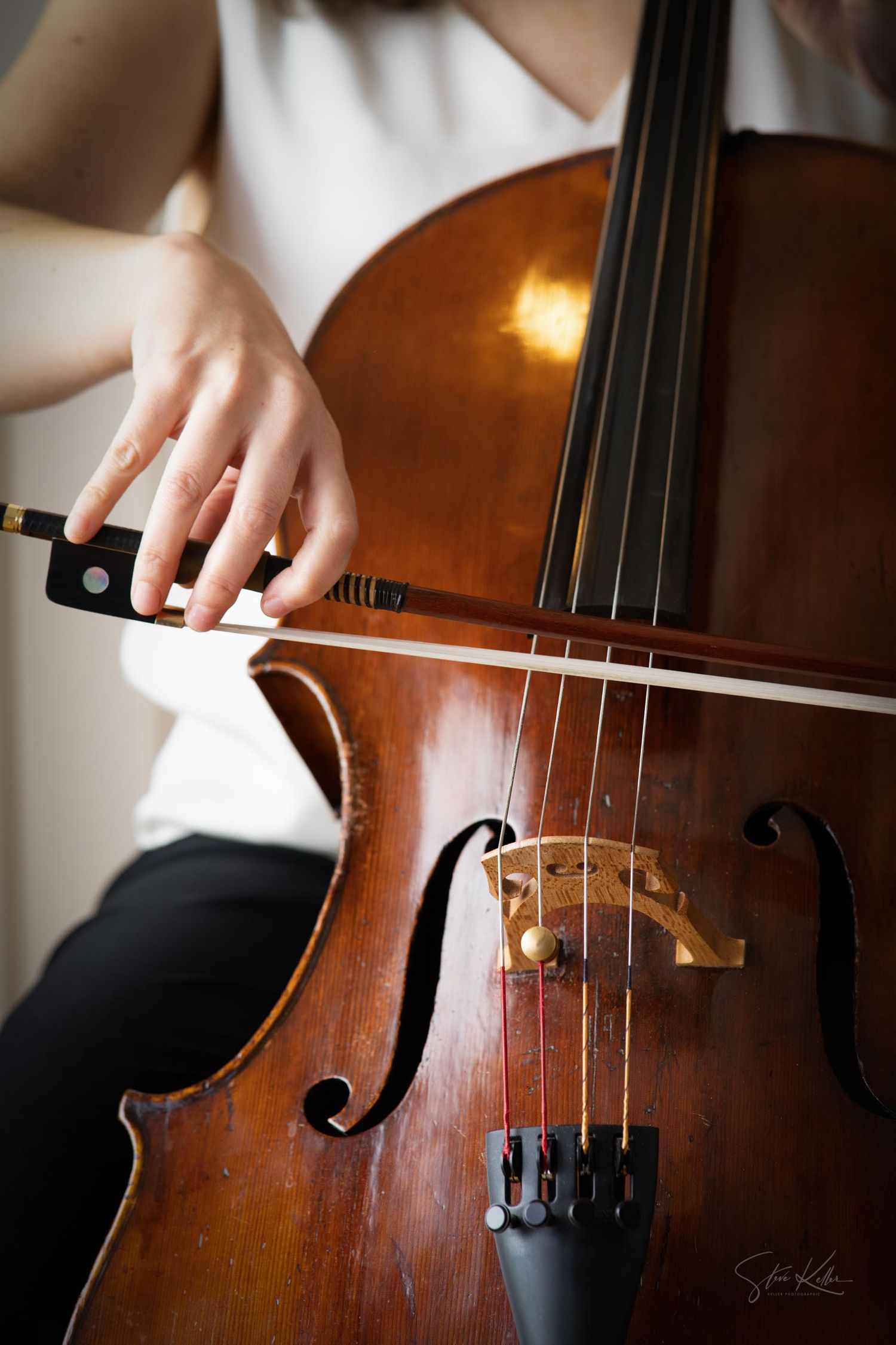 Close-up details of a wooden cello being played, showing the bridge, strings, and f-holes in warm lighting.