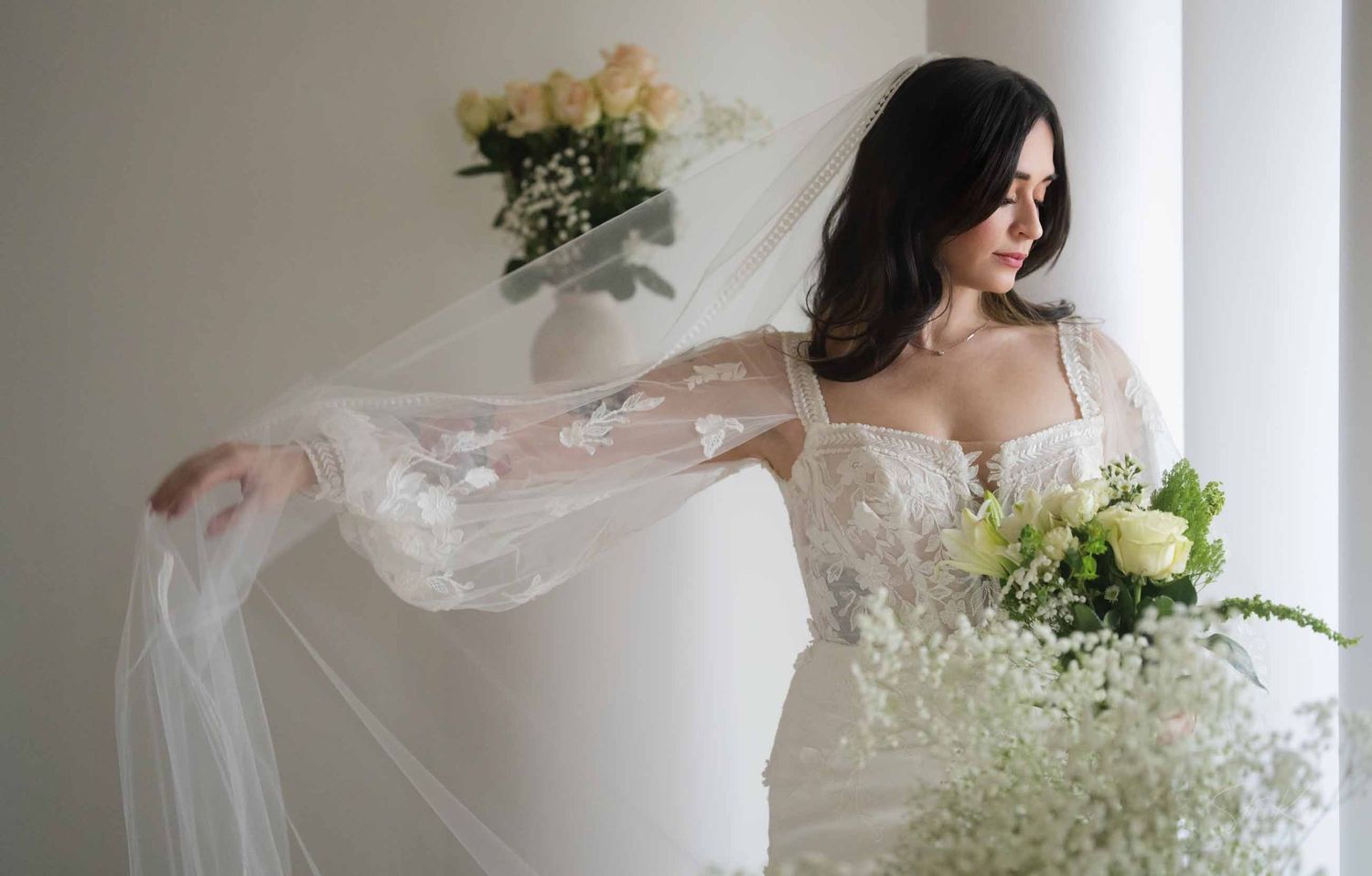 A flowing white wedding dress and veil create an ethereal silhouette against a light background.