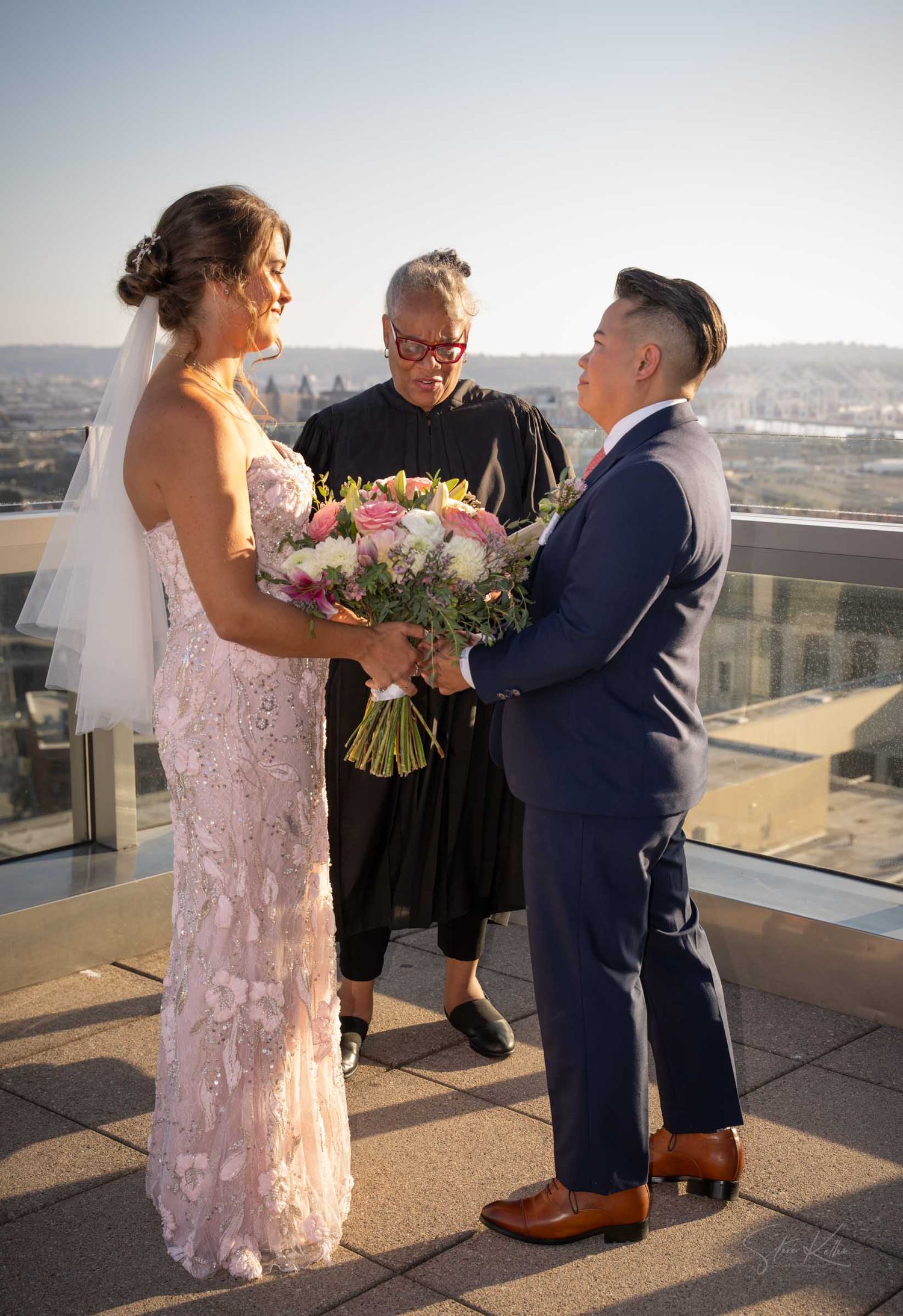 Bride and groom exchange vows on a rooftop with city skyline views with officiant.