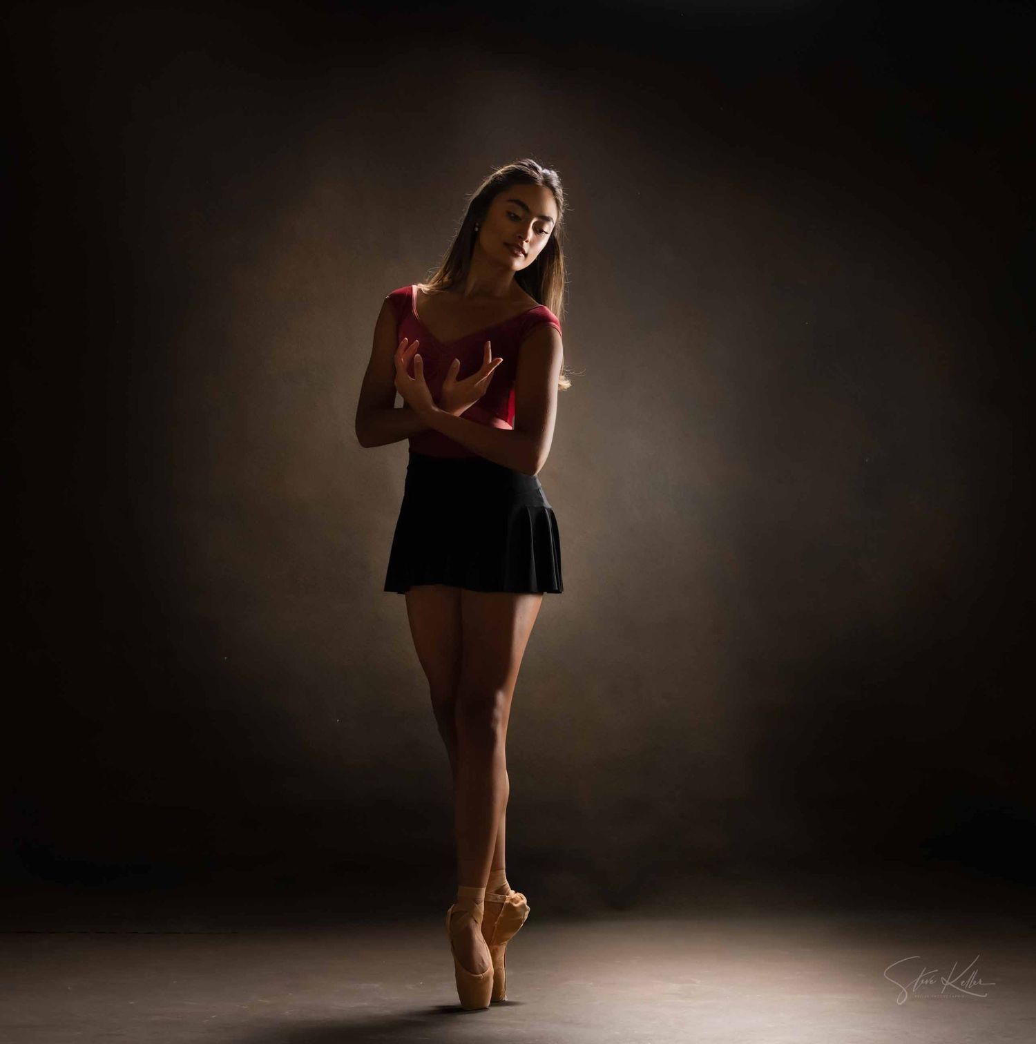 A figure in red performs a graceful dance pose against a dark background, creating a dramatic silhouette effect.