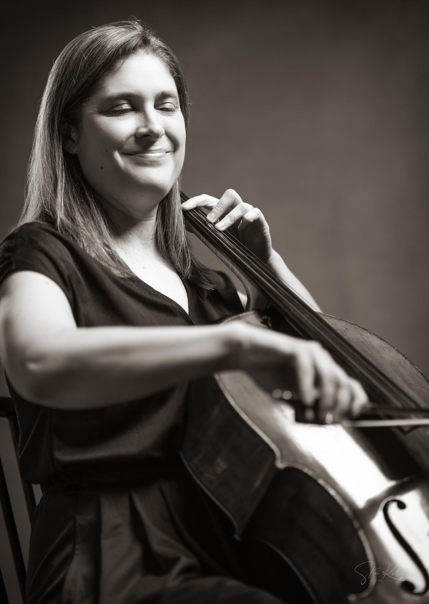 Black and white photo of a musician performing with a cello while smiling expressively during a performance.